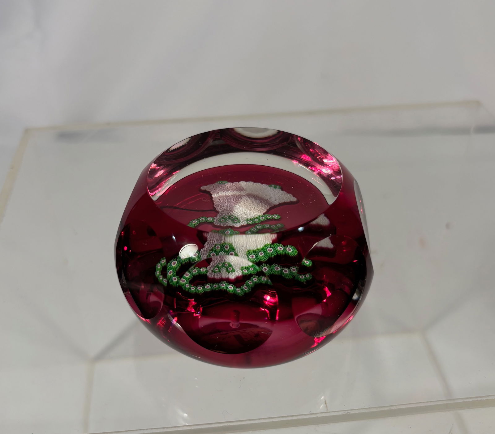 Perthshire Paperweight, Scotland, Ruby Red Glass Floral Design: Perthshire paperweight, Scotland, featuring a floral motif encased within deep ruby red glass. The paperweight retains the original Perthshire Paperweights label on the polished base.Height: 2 inches.