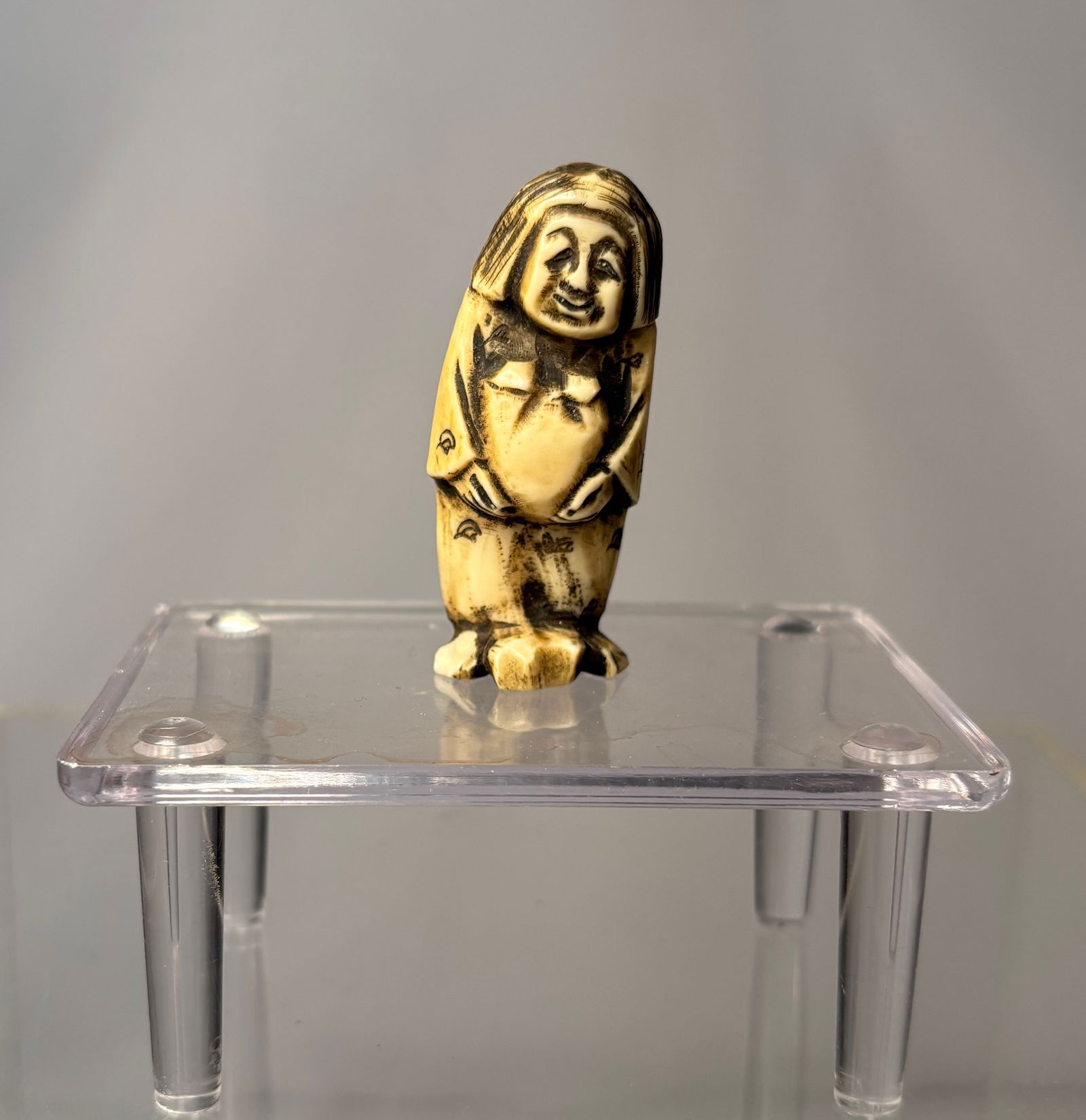 A Japanese Figural Netsuke, Carved Bone Standing Figure, Signed (Hisakazu / Ky?ichi), Meiji period: 19th century, A Japanese figural netsuke carved from bone, depicting a standing human figure with a humorous expression and stylized features. The carving includes two himotoshi to the reverse, confir