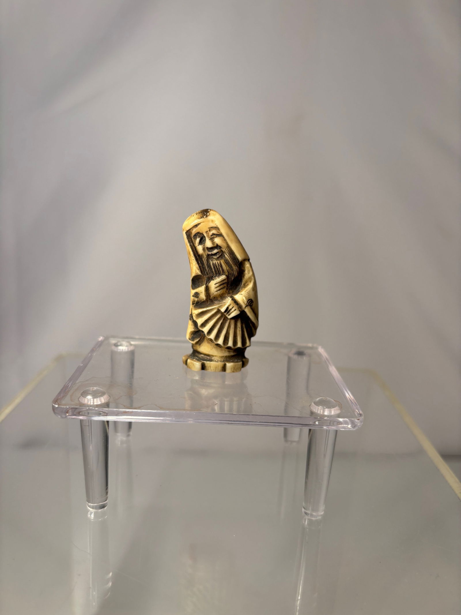 A Japanese Figural Netsuke, Carved Bone Standing Figure, Signed (Hisakazu / Ky?ichi): 19th century, A Japanese figural netsuke carved from bone, depicting a standing human figure with a humorous expression and stylized features. The carving includes two himotoshi to the reverse, confir