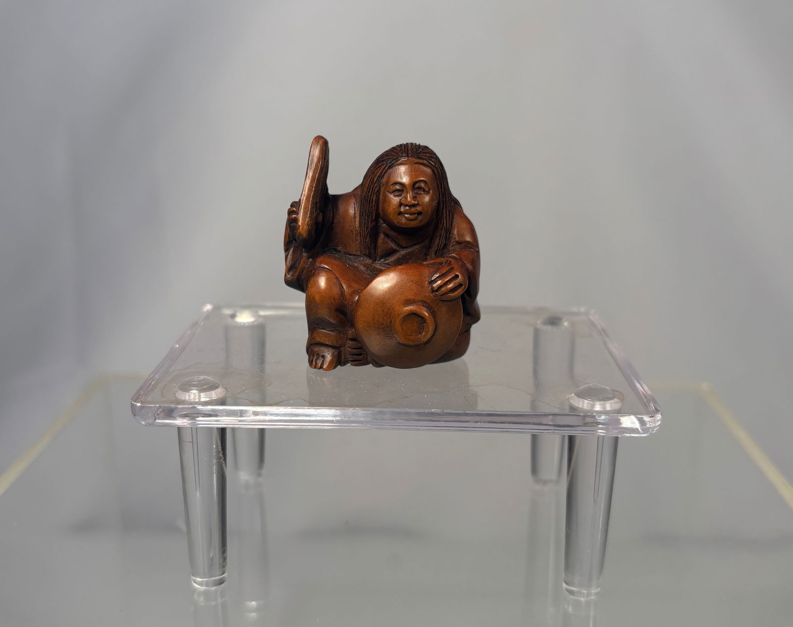 A Japanese Boxwood Netsuke, Figure with Jar, Signed Ishikawa,: Meiji period (19th century), A finely carved Japanese boxwood netsuke depicting a seated figure holding a jar, rendered with a warm patina and expressive facial features. The carving shows careful att