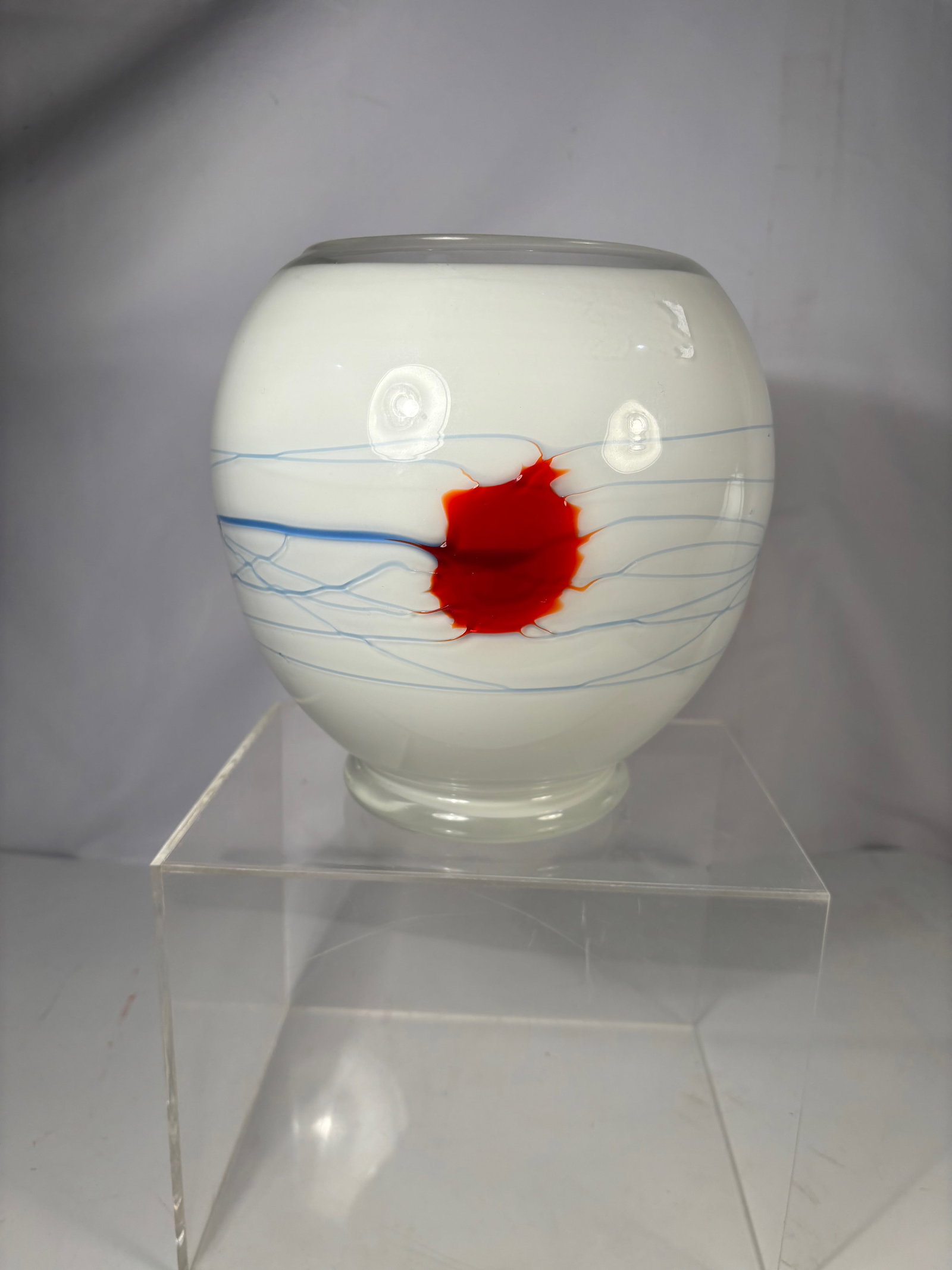 A Studio Art Glass Vase with Red Core and Blue Thread Decoration: Contemporary art glass vase of rounded form with frosted white ground. The body is decorated with internal blue thread-like lines and a central red abstract motif, encased within the glass. Raised on