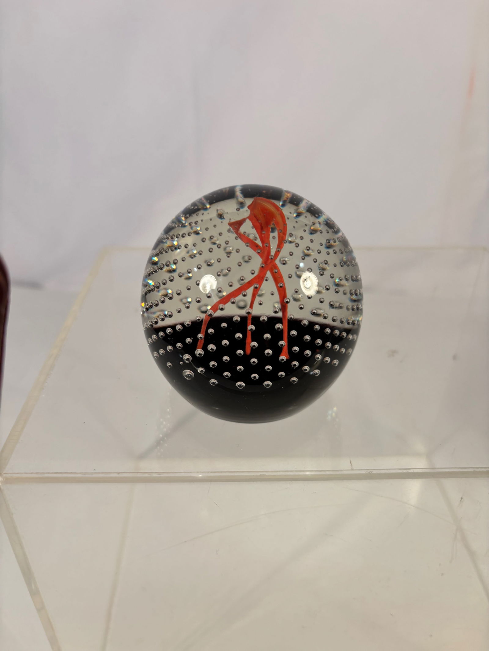 An Art Glass Paperweight with Red Ribbon and Controlled Bubble Ground: Art glass paperweight featuring an abstract flowing red ribbon form suspended within a clear dome over a black ground. The interior is decorated with dense controlled air bubbles, creating a dynamic,