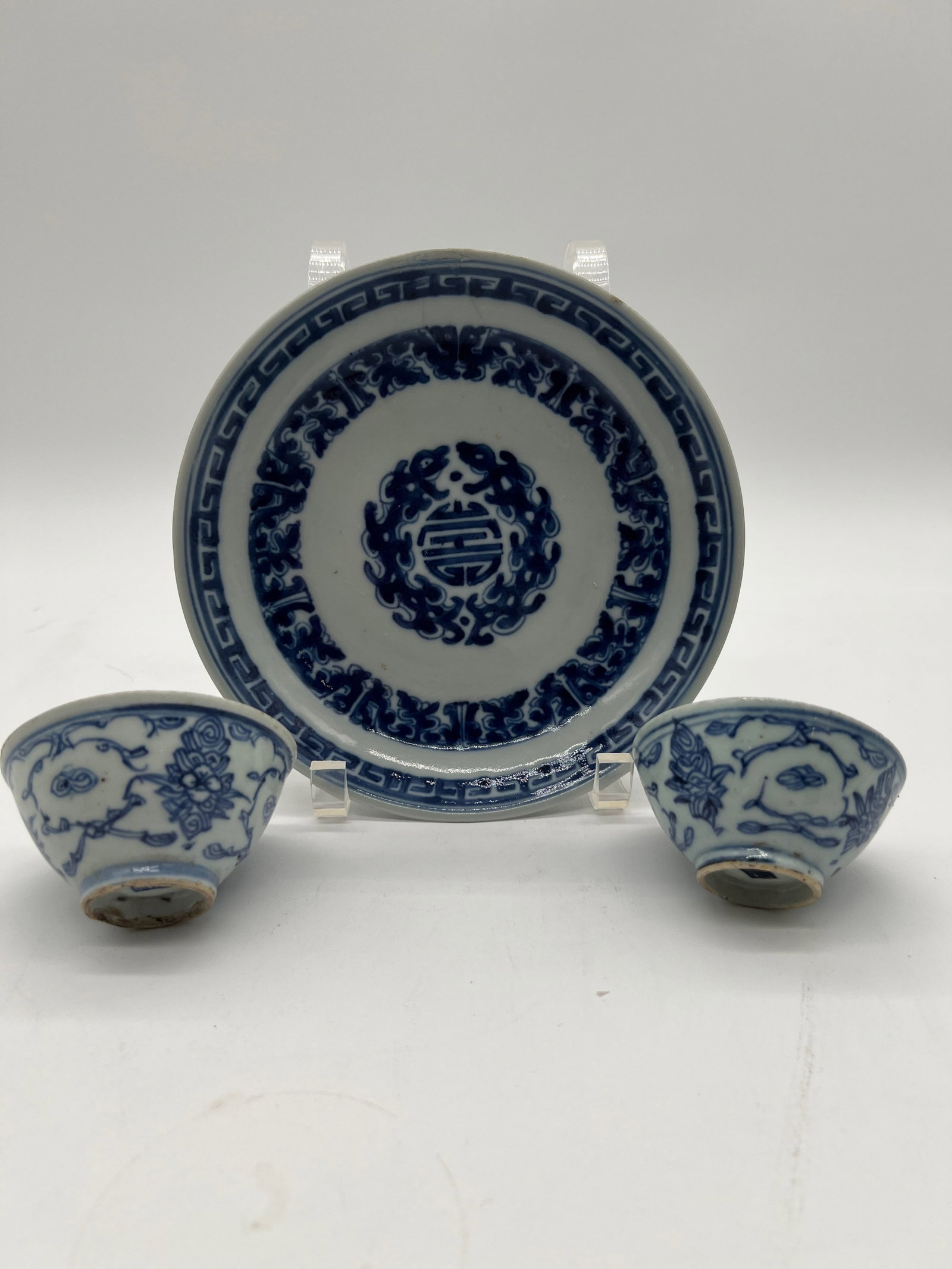 A Chinese blue and white porcelain plate with 2 cups: Qing dynasty (1644-1912); The plate has a central medallion with a Chinese character or symbol; The areas surrounding the central medallion and the rim display stylized floral or scroll patterns; The