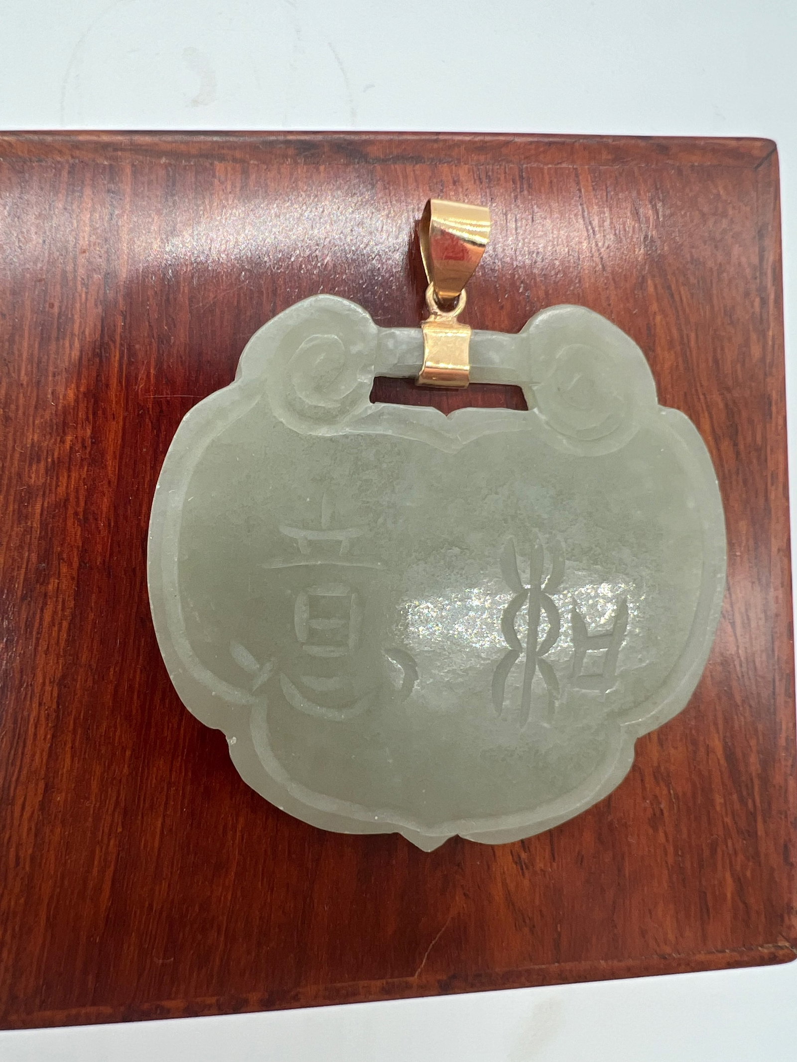 A Chinese celadon jade Ruyi pendant with 14k gold clasp: Qing dynasty (1644-1912); The Chinese characters engraved on the jade are likely auspicious phrases or symbolic words. These types of carvings often carry meanings of blessings, peace, or luck. Dimens