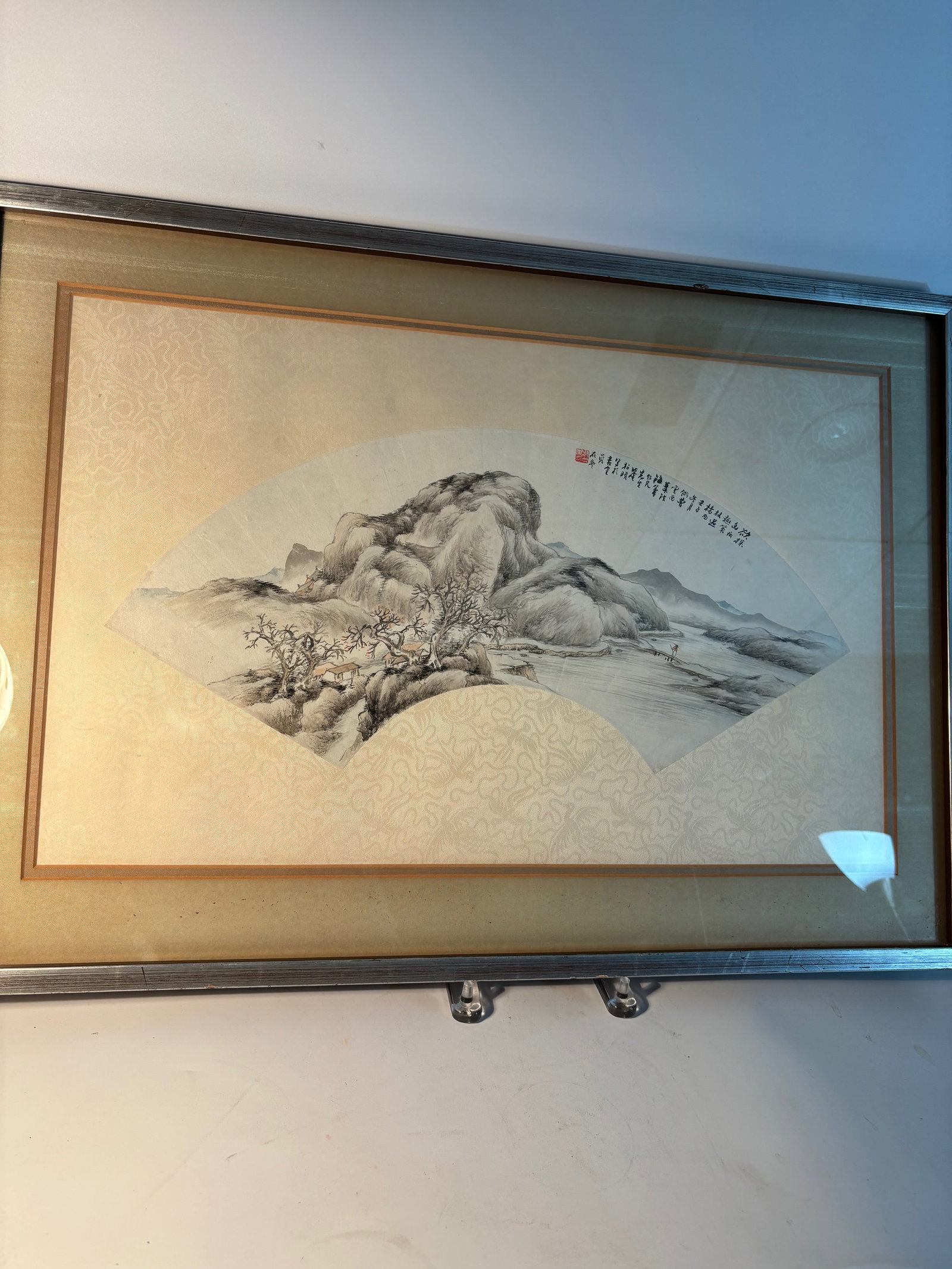 A Framed Chinese Fan-Shaped Ink Landscape Painting with Calligraphy and signature: Qing Dynasty(1644-1912); A traditional Chinese ink landscape painting in a fan-shaped composition, mounted within a silk brocade mat and wooden frame. Executed in black ink with subtle tonal variation