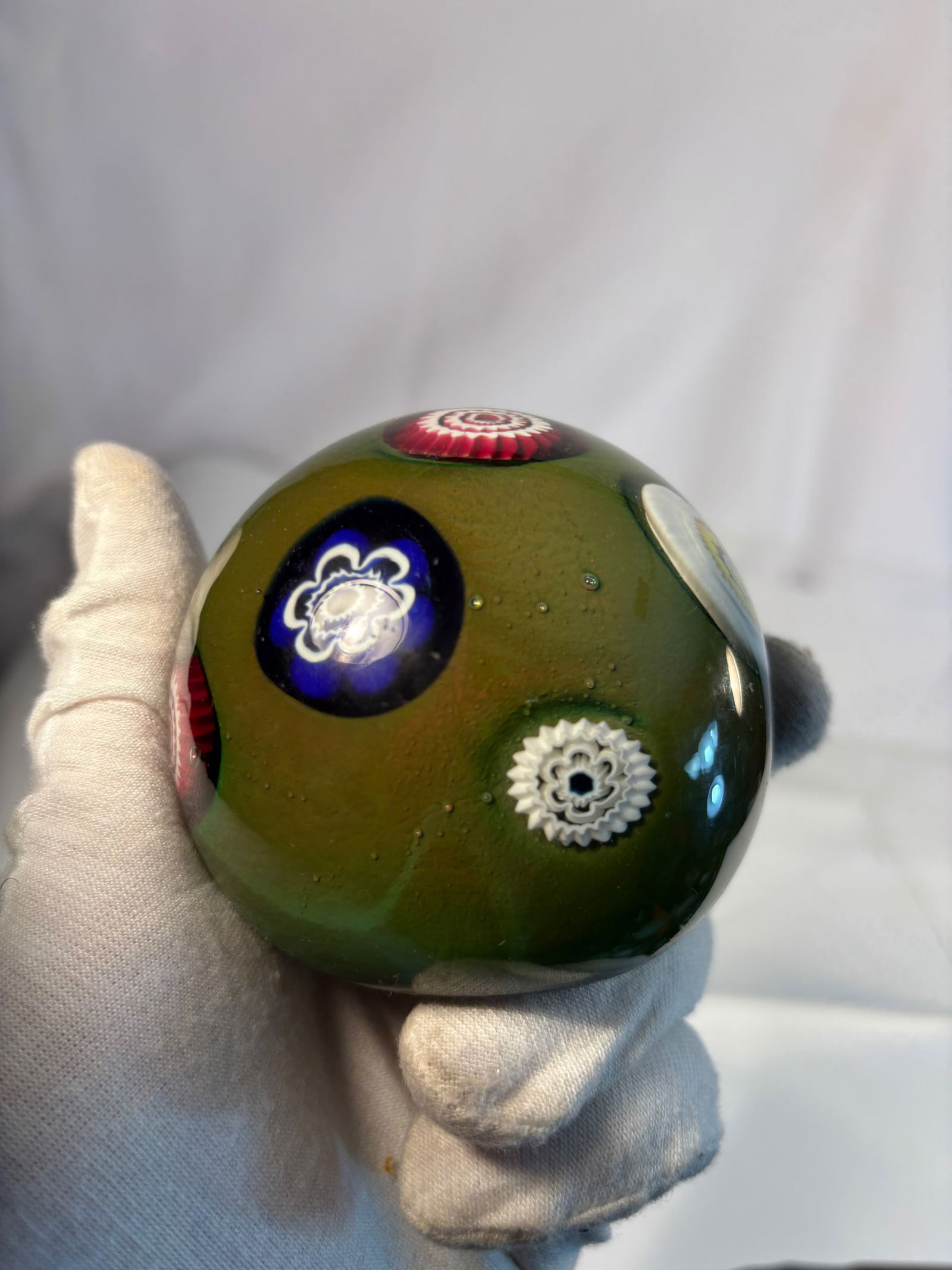 Italian Murano Millefiori Art Glass Paperweight, Mid-20th Century: A fine Murano art glass paperweight of spherical form, featuring multicolored millefiori canes in concentric floral patterns set within a translucent olive-green ground. The base with a polished ponti