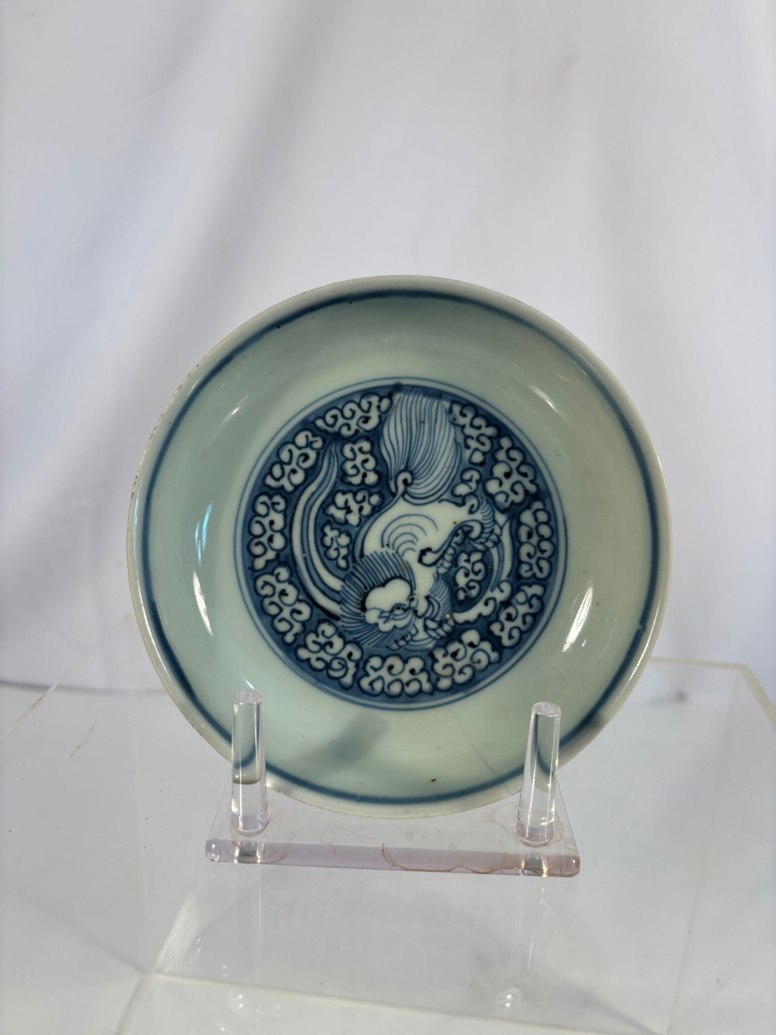 A Chinese Blue and White porcelain ‘Lion Among Clouds’ Dish Ming Dynasty, Tianqi Period: The dish is delicately potted with rounded sides rising from a short foot to an everted rim. The interior finely painted in vivid underglaze cobalt blue with a Buddhist lion (Foo Dog) frolicking among