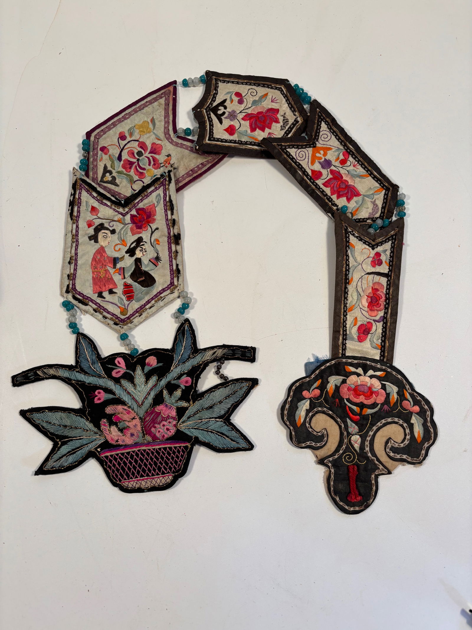 A Chinese silk embroidered ceremonial chain: 19th century;Figures in garden scenes, floral motifs, and auspicious symbols (like peaches, lotuses, and peonies) .Dimensions? Length: 35 inches.