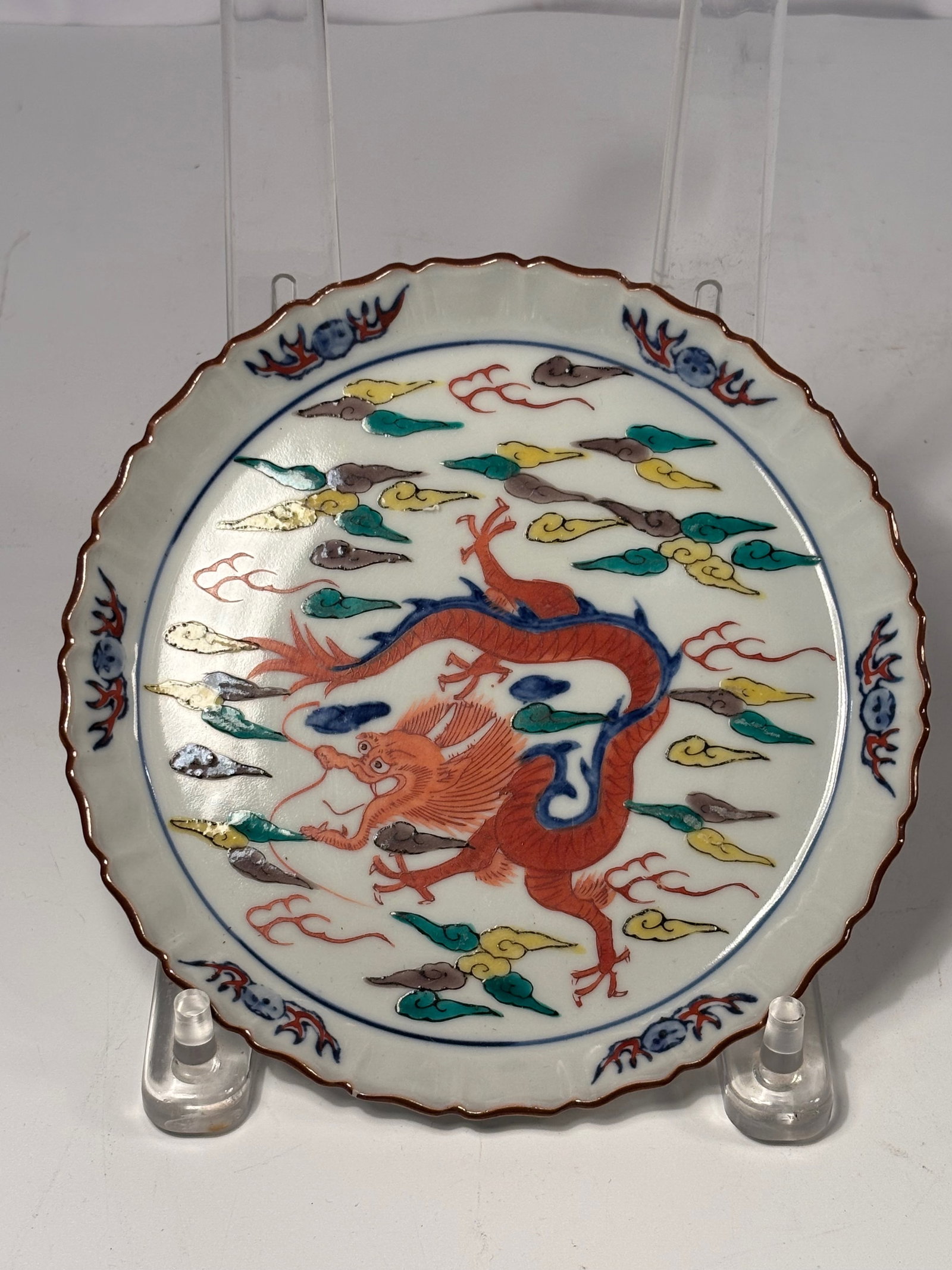 Japanese Kutani Porcelain Plate with Dragon Design, Marked “Da Ming Xuande Nian Zhi: Late Meiji to Early Sh?wa Period (circa 1900–1950); A Japanese Kutani porcelain plate finely hand-painted with a vibrant red dragon among multicolored swirling clouds. The scalloped rim is accented