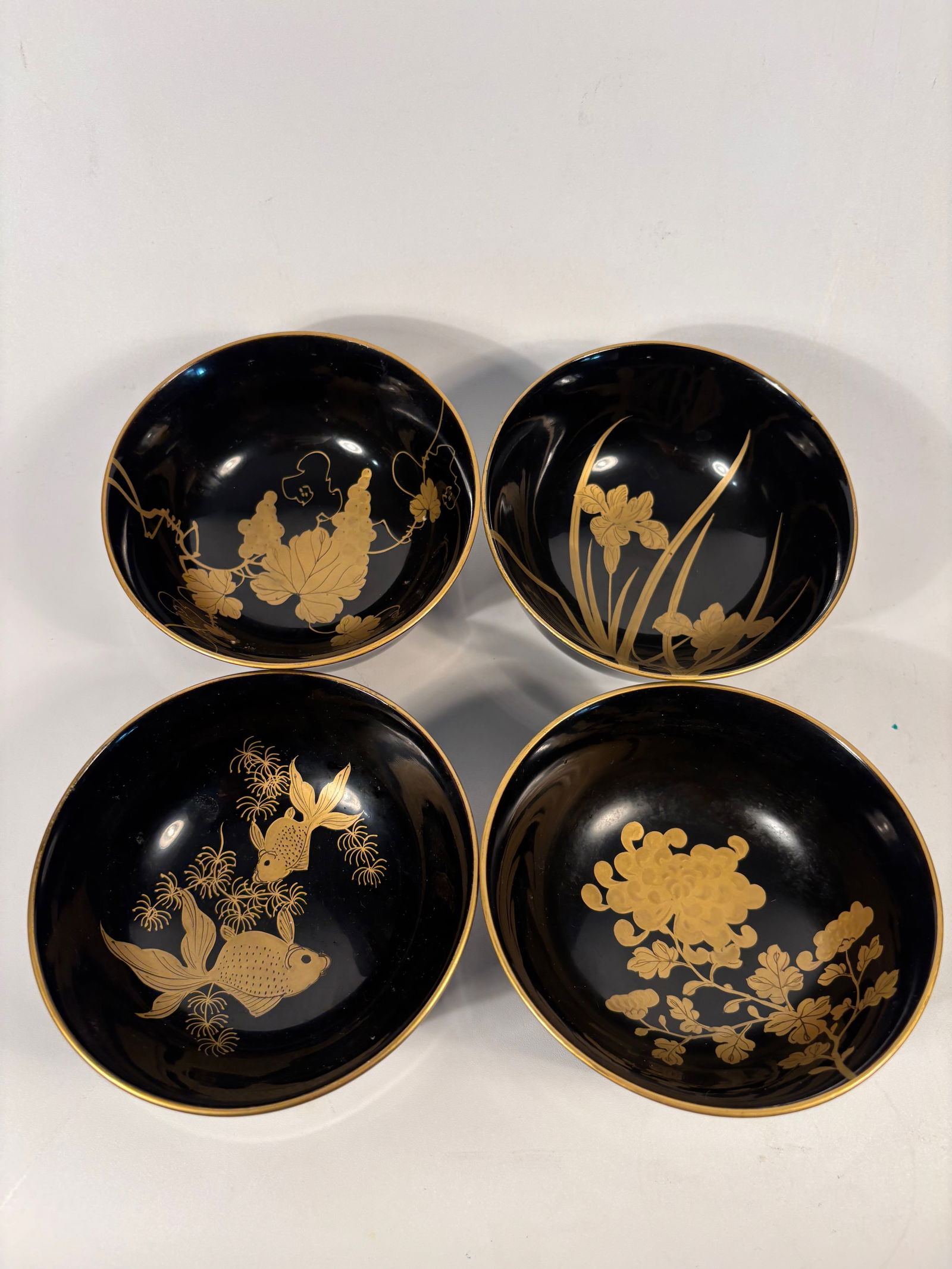 Set of 4 Japanese Makie Lacquer Bowls: Each bowl finely decorated in gold maki-e on black lacquer with traditional Japanese motifs including plum blossoms, cranes in flight, butterflies, and flowering vines. The designs are delicately rend