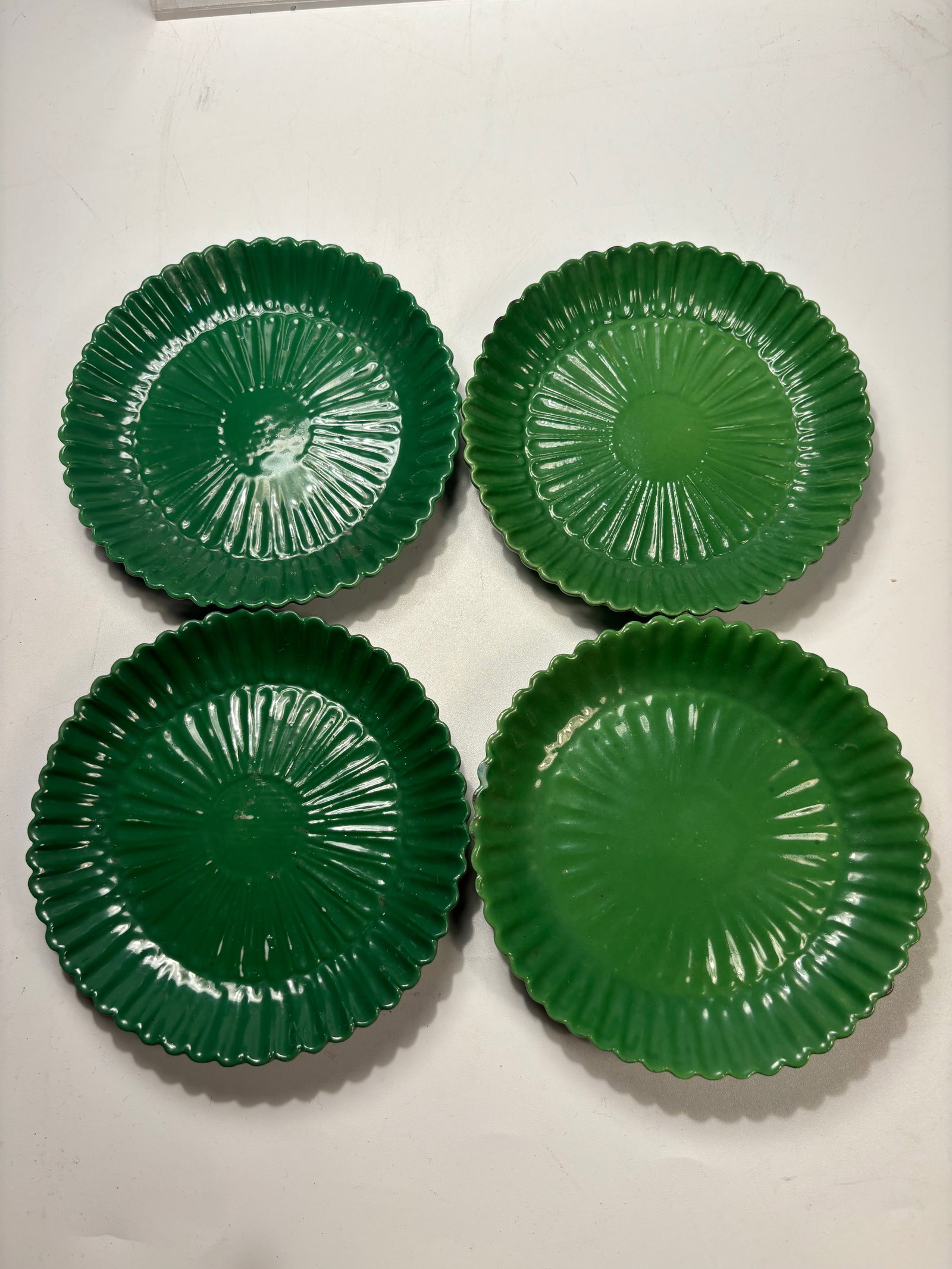Set of Four Italian Green-Glazed Ceramic Dishes: A set of four Italian green-glazed ceramic dishes, each molded with radiating rib decoration and a scalloped rim. The bases are marked “ITALY.” The pieces display a glossy green glaze with sli