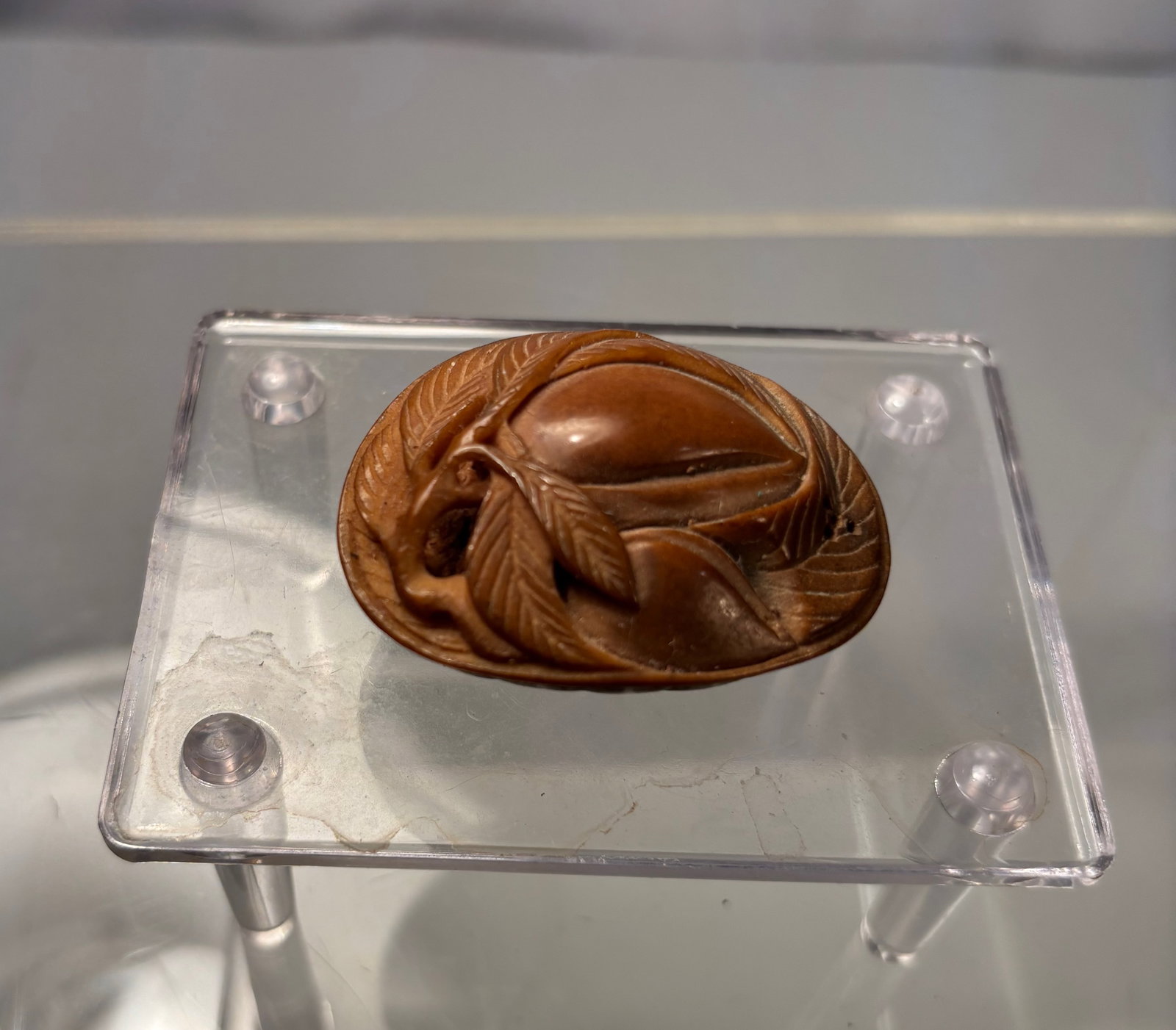 A Japanese Carved Bone Netsuke with Fruit and Leaf Motif: Japanese hand-carved wood netsuke, modeled as a fruit surrounded by stylized leaves. The underside is pierced with two himotoshi, consistent with traditional functional netsuke used to secure sagemono