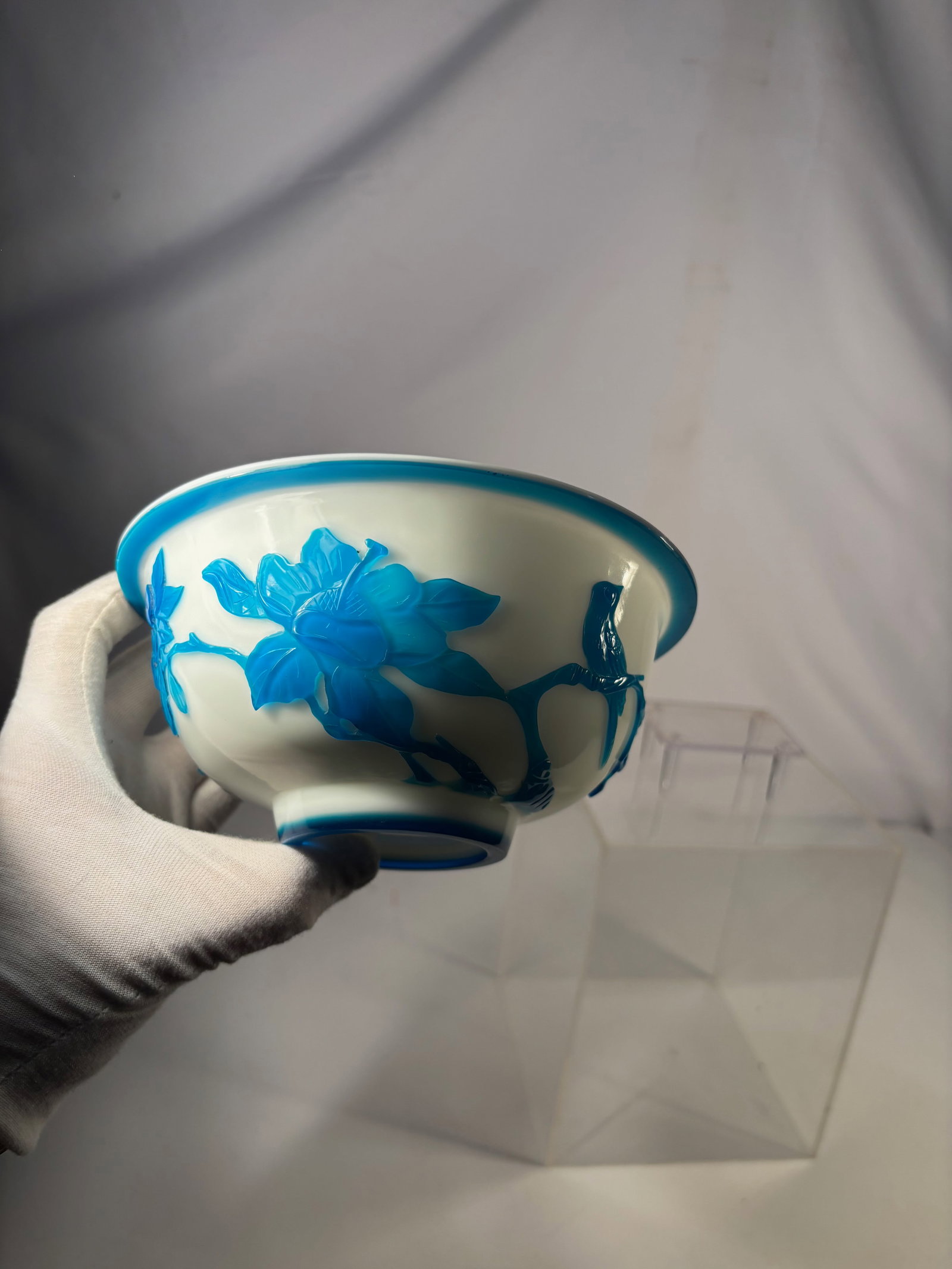 A Chinese Blue Overlay Peking Glass Bowl: Qing Dynasty (1644-1912); Chinese blue overlay glass bowl, featuring a translucent clear body overlaid with deep cobalt-blue glass, decorated with stylized floral motifs. The bowl has a rounded form w