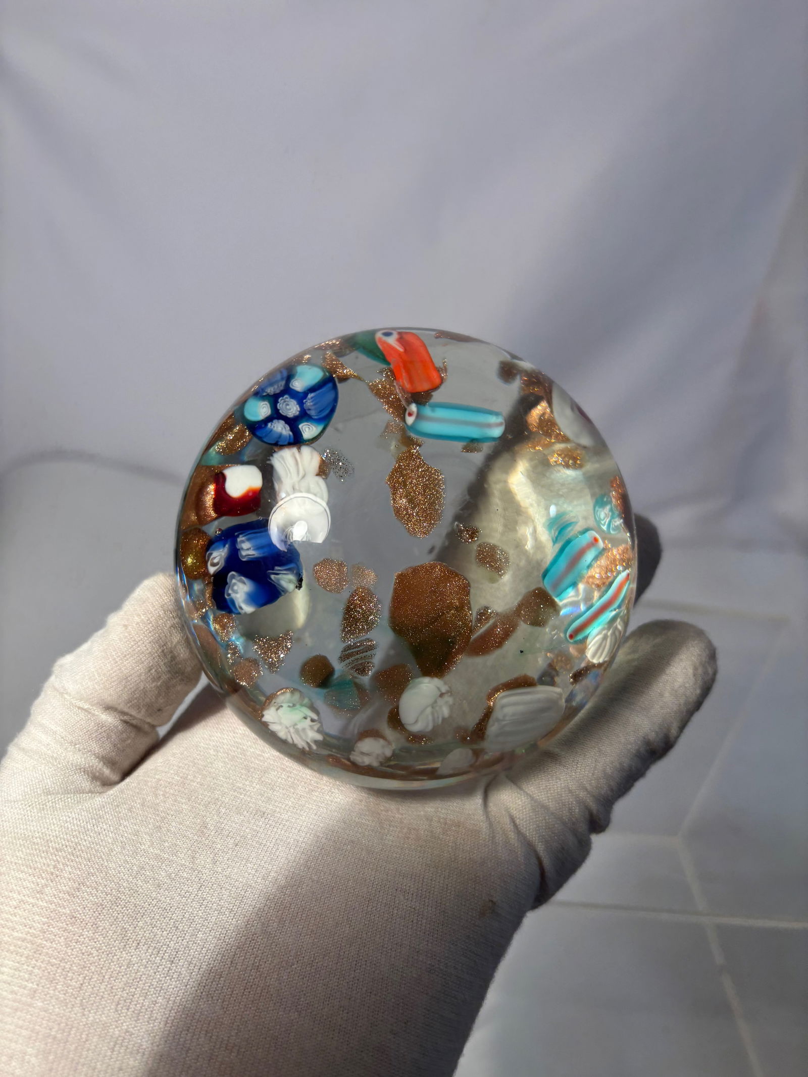 A Murano Art Glass Paperweight with Millefiori and Aventurine, Italy: Hand-blown Murano art glass paperweight, made in Italy, featuring embedded millefiori canes in blue, red, and white, accented with rich coppery aventurine inclusions throughout the clear glass body. T