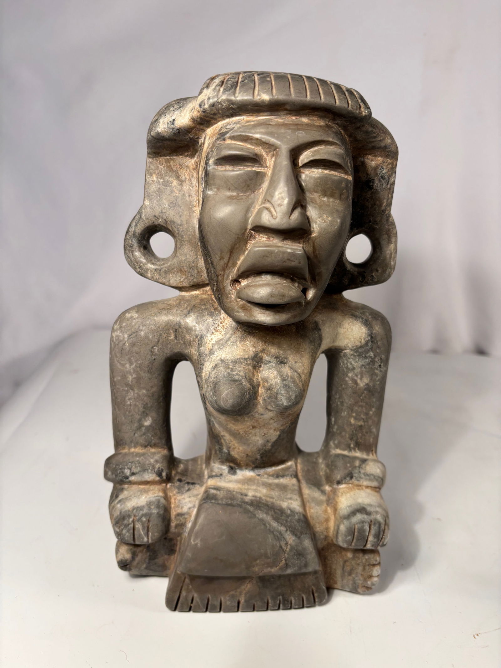 Pre-Columbian Style Stone Carved seated Abstract Figure with Pierced Openings: A carved dark stone abstract figure, formed with a stylized head and body featuring multiple pierced openings. The sculpture presents a bold geometric silhouette with softened edges and natural surfac