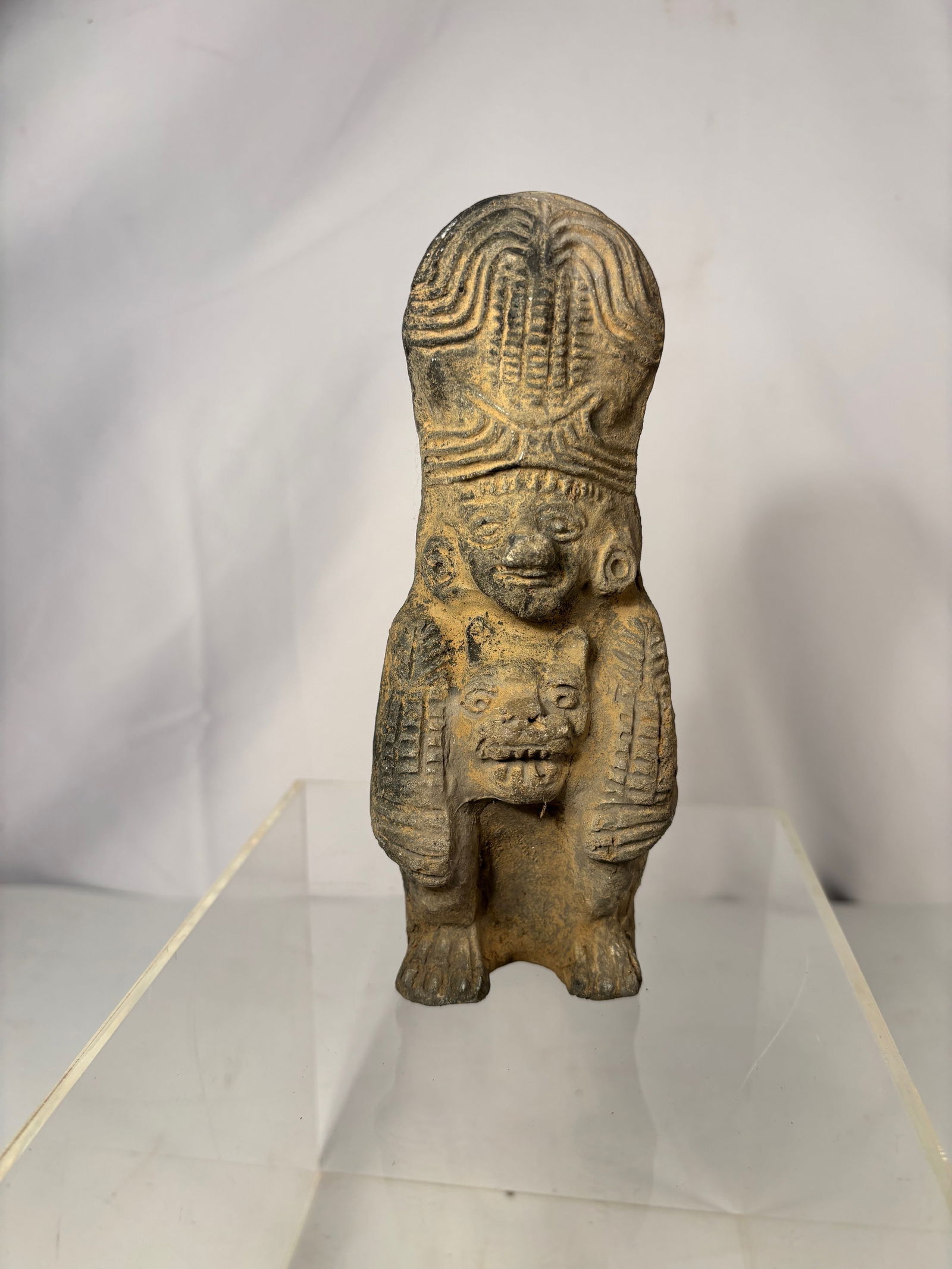 Pre-Columbian Style Hollow-Back Terracotta Figure: Terracotta figure in the style of ancient Pre-Columbian Mesoamerican art, depicting a standing figure with a tall, stylized headdress and carved decorative details. The figure holds an animal-like cre