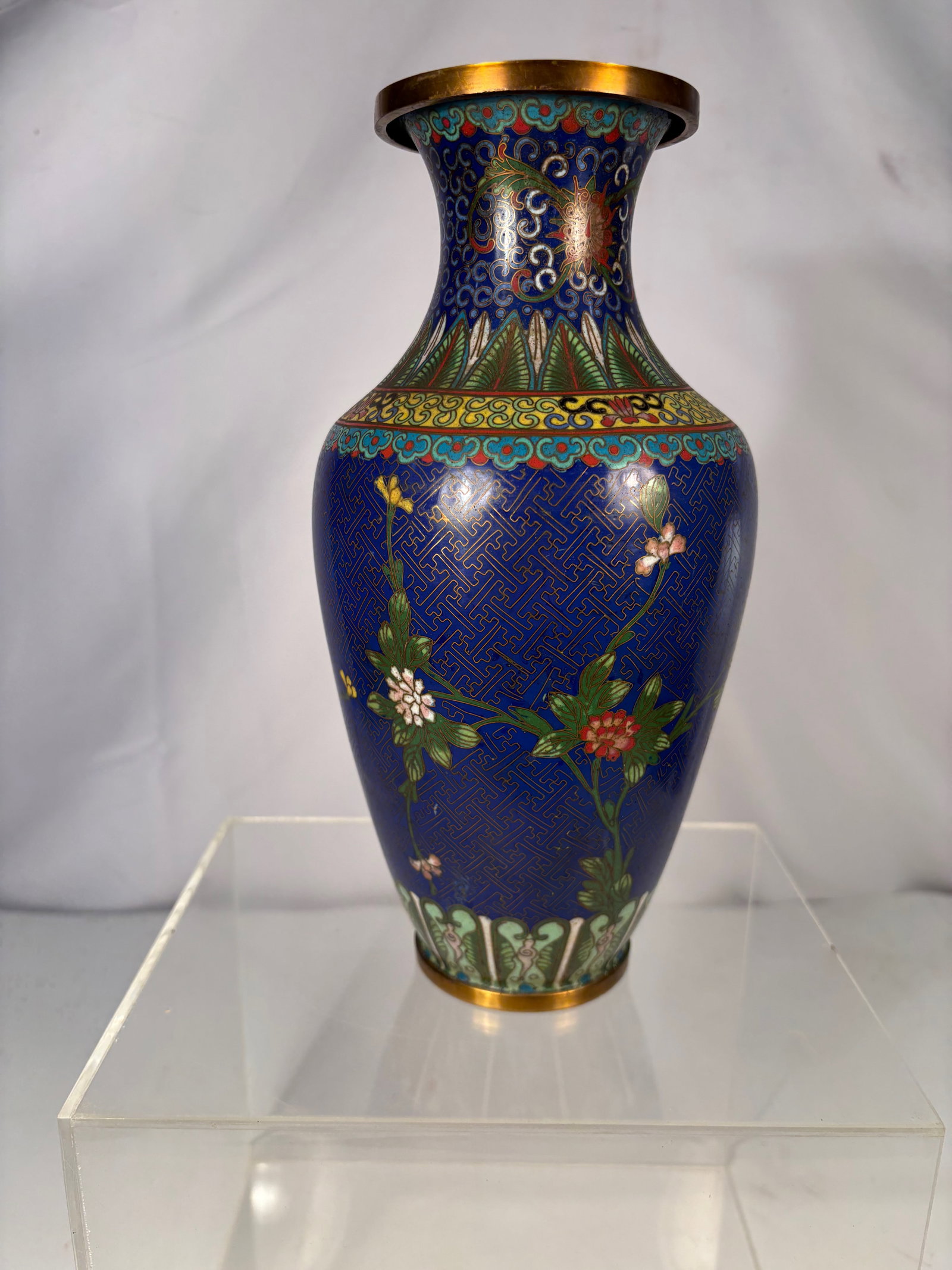 A Chinese Cloisonné Enamel Vase with Floral Decoration: Chinese cloisonné enamel vase with cobalt blue ground, decorated with floral and scrolling motifs in multicolor enamel. The rim mounted with a gilt metal collar. Height: 10 inches