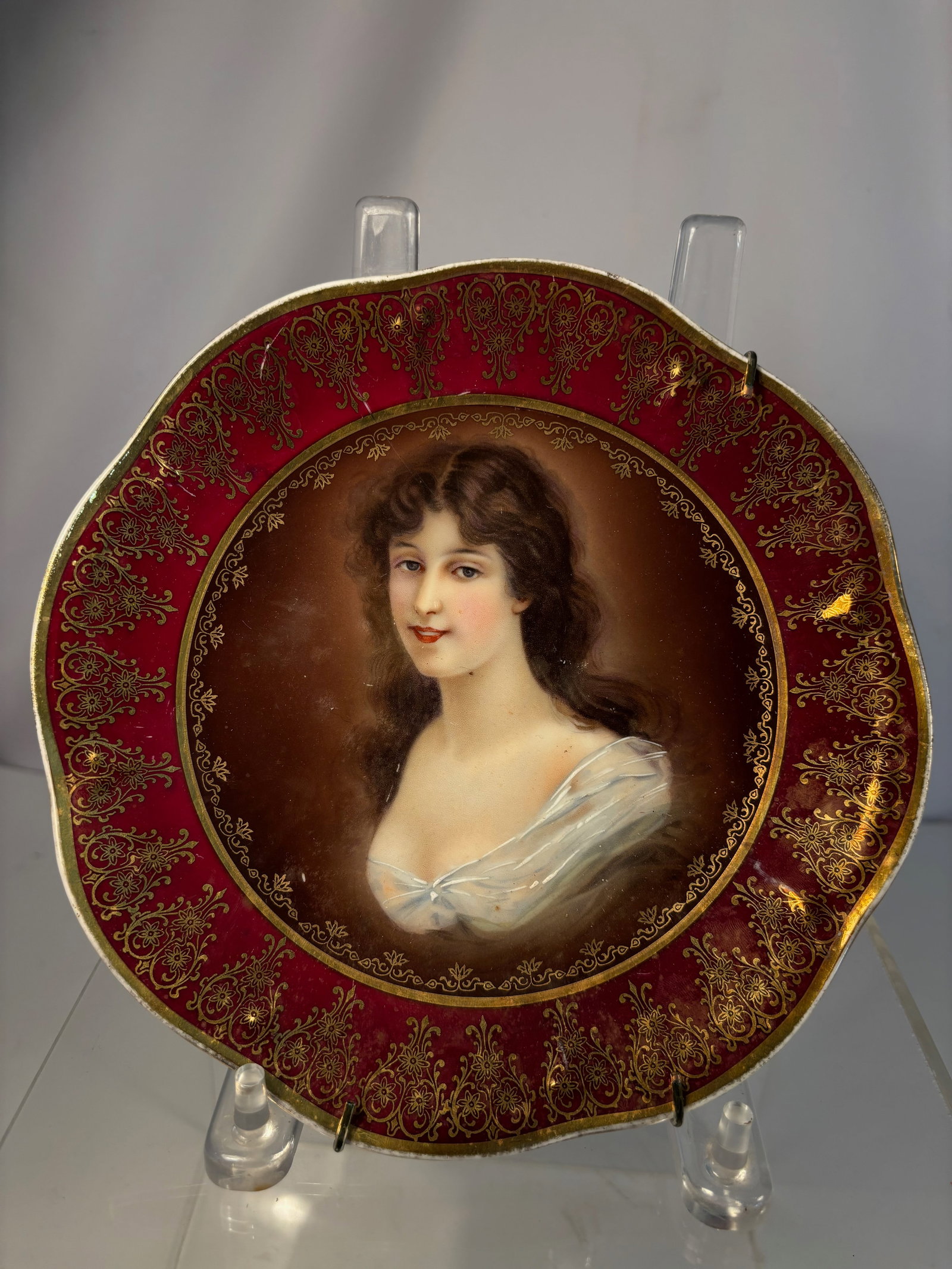 Royal Vienna-Style Hand-Painted Porcelain Portrait Plate, Signed, with C&I Mark, circa 1930: A fine Royal Vienna-style porcelain portrait plate, featuring a hand-painted half-length portrait of a young woman with brown hair and white drapery, set against a warm brown background. The rim decor