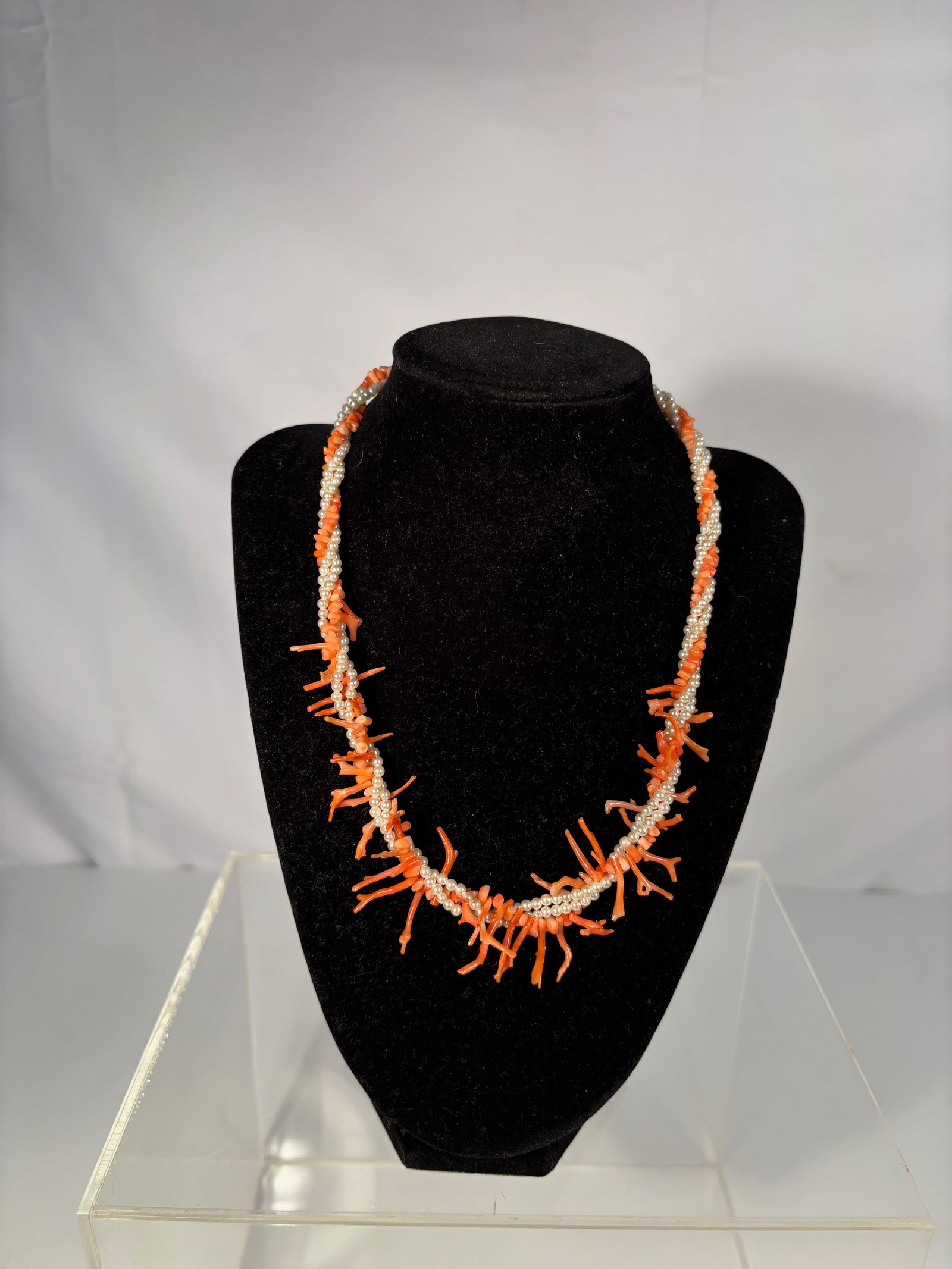 Twisted Strand Necklace of Coral Branches and Seed Pearls with Gilt Clasp: A vintage twisted necklace composed of natural orange-red coral branches entwined with small white seed pearls, secured with an engraved gilt oval fishhook clasp. This lively combination of pearls and