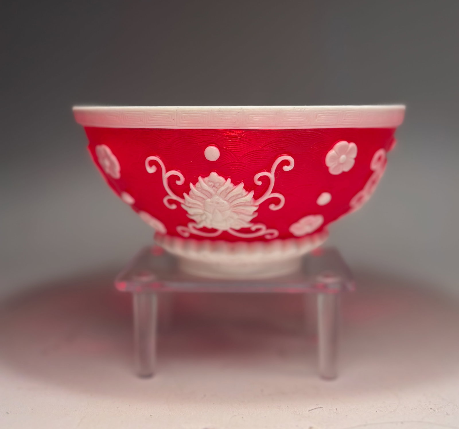 A Chinese Peking Overlay Glass Bowl with "QIANLONG" mark: 19TH century or later,Finely crafted in translucent ruby red glass overlaid with opaque white glass, the bowl is decorated in high relief with stylized chrysanthemum blossoms and scrolling tendrils, a