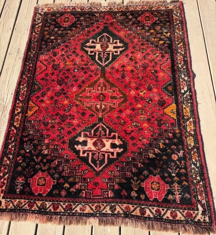 Mid-20th century Persian tribal hand knotted 100% wool rug: Triple medallion layout with bold geometric motifs.The field is filled with scattered small floral and animal forms, a hallmark of Qashqai symbolism.The deep red and dark blue/black tones are common i