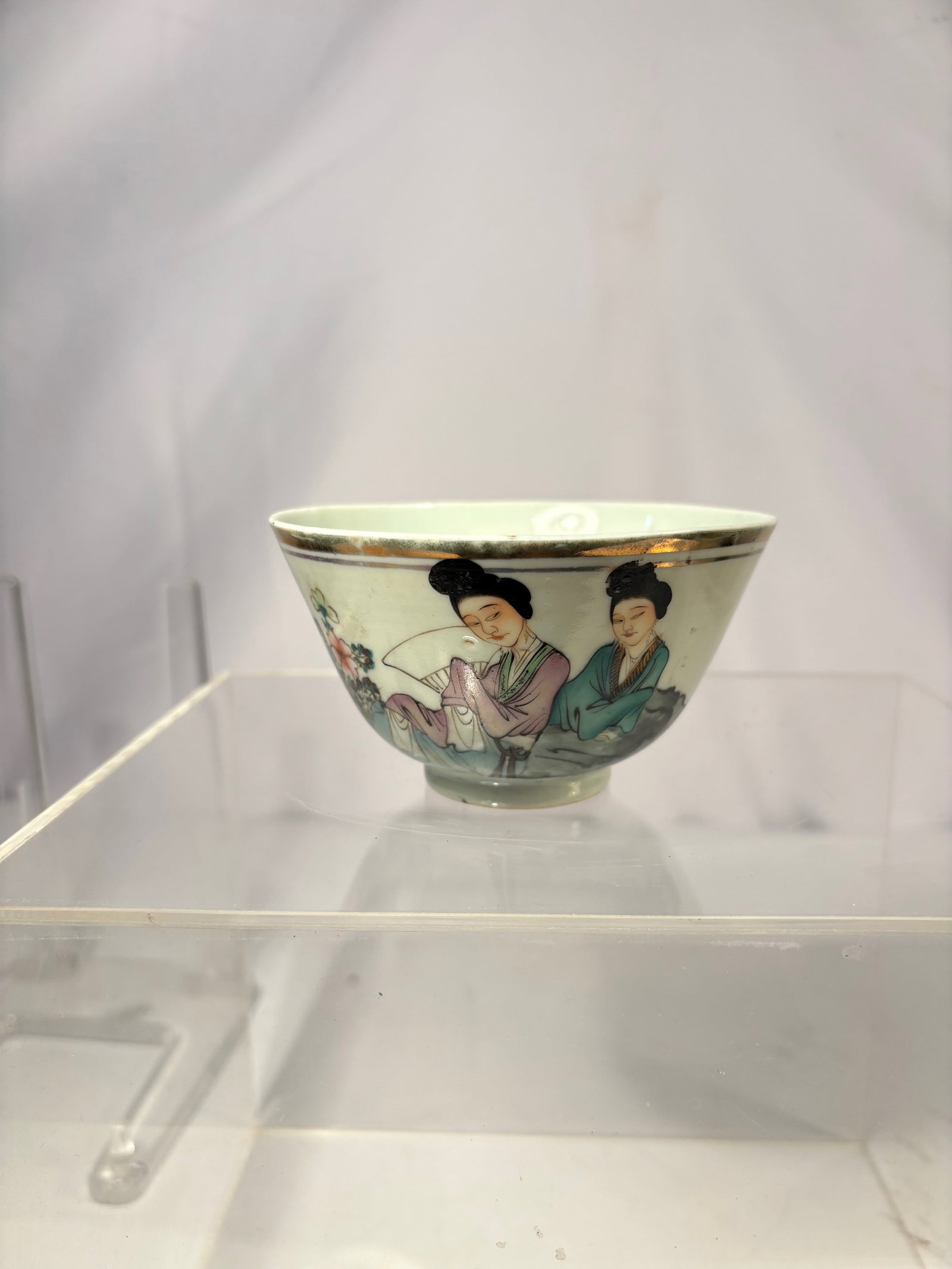A Chinese Famille Rose Figural Bowl, Mark of “Jiangxi Yichun Ci Zuo: Early 20th century; A finely hand-painted famille rose porcelain bowl, decorated with two elegant ladies seated among rocks, holding fans and accompanied by blooming flowers. The figures are rendered