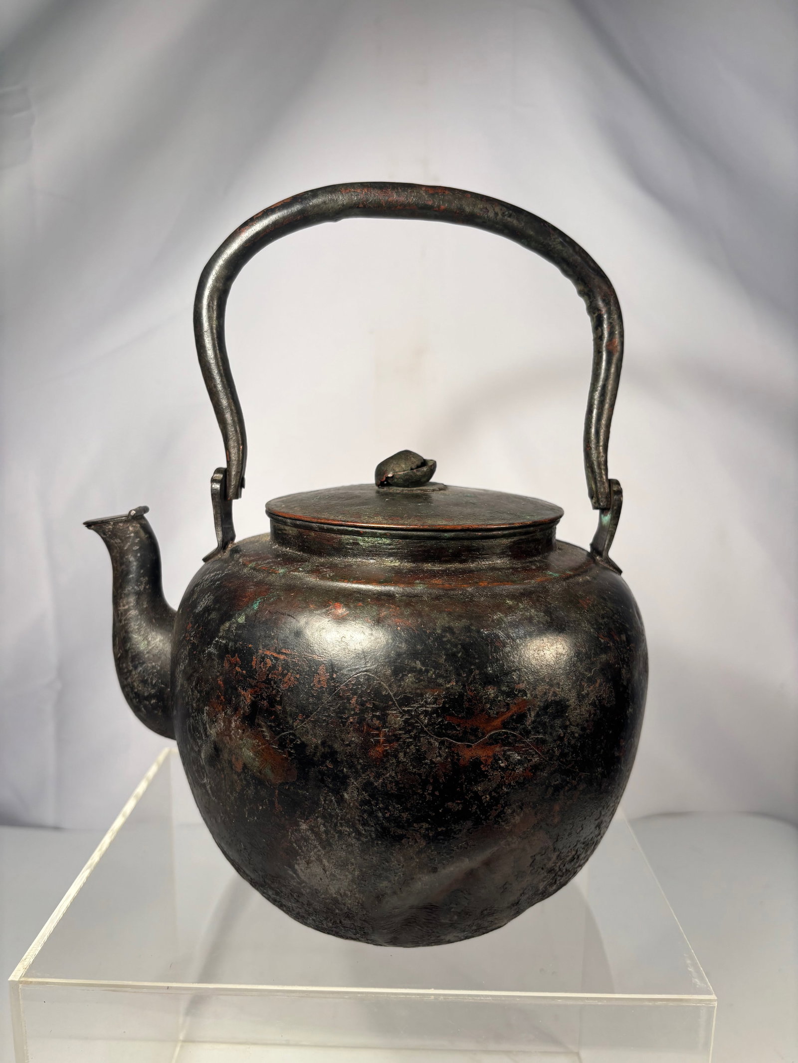 A Japanese Hand-Hammered Copper Yakan (Kettle), 8.5 in. Diameter: Probably Early Edo (circa 1650–1750); A superb early Japanese hand-hammered copper yakan of rounded form with arched handle and short spout, richly oxidized surface showing centuries-old patina of b