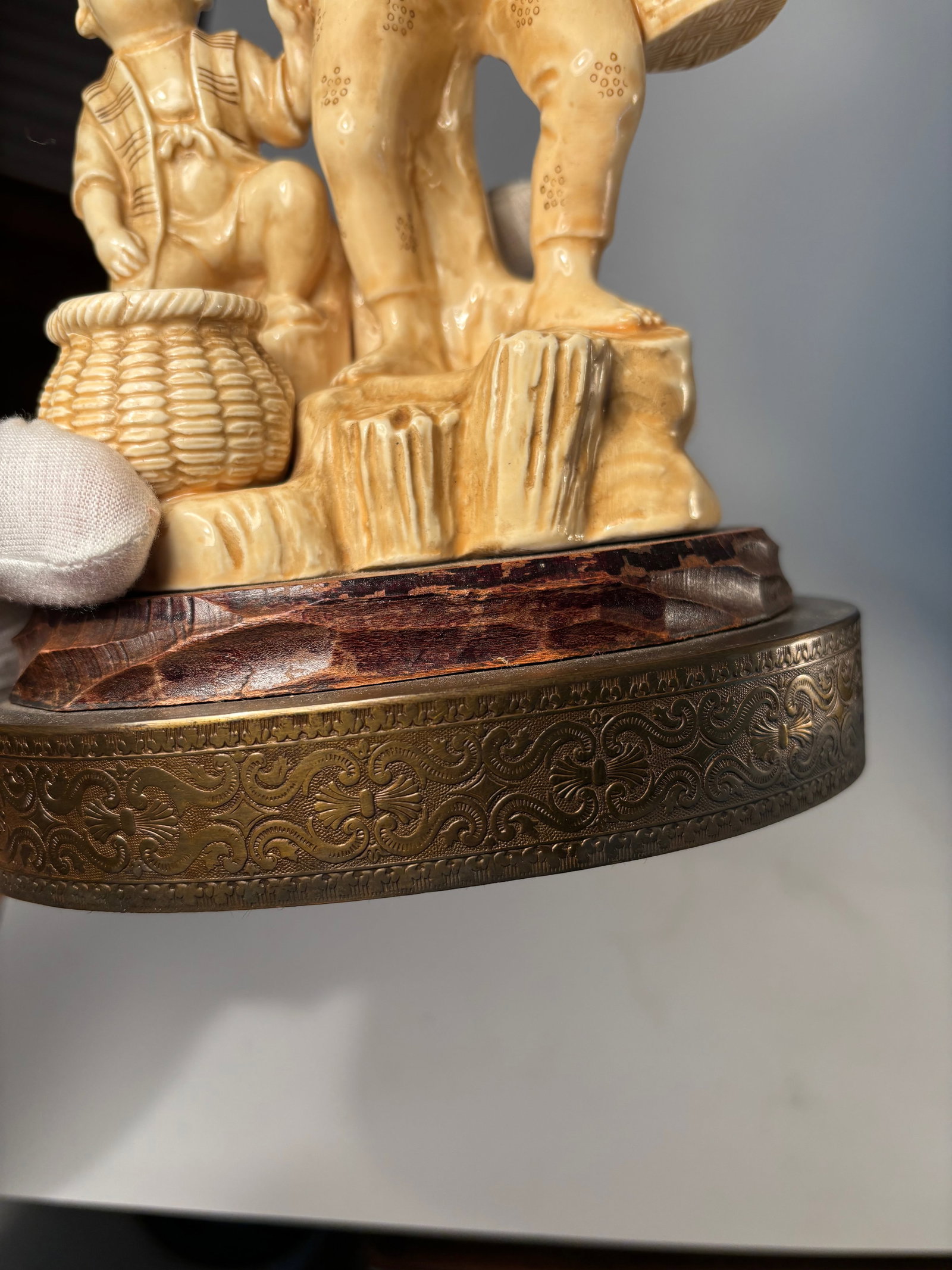 A Japanese Moriyama porcelain statue of woman and child: LATE 19TH, EARLY 20TH Century; Depicting a standing woman in kimono holding a rooster, accompanied by a small child holding a bowl. A large woven-style basket sits between them on a rocky base, all mo