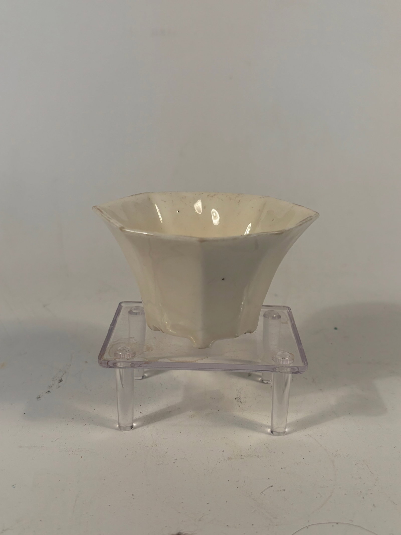 A Chinese Blanc-de-Chine Hexagonal Cup: Qing dynasty(1644-1912); Of faceted hexagonal form with six bracket-lobed sides, raised on three short ruyi-form feet. The glossy white glaze typical of Dehua ware. An impressed or incised mark to the