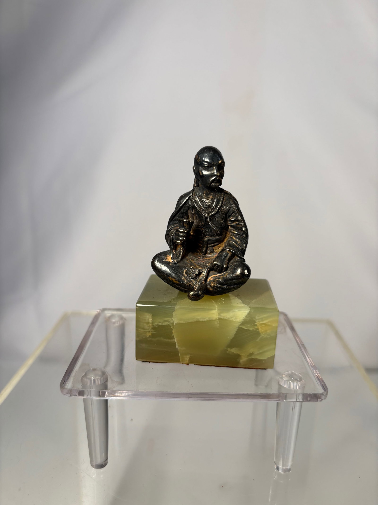 A Silver Figure of a Seated Man on Stone Base: Small silver figure depicting a seated man, modeled with flowing robes and detailed facial features, mounted on a rectangular stone base. The figure displays a darkened patina consistent with age and