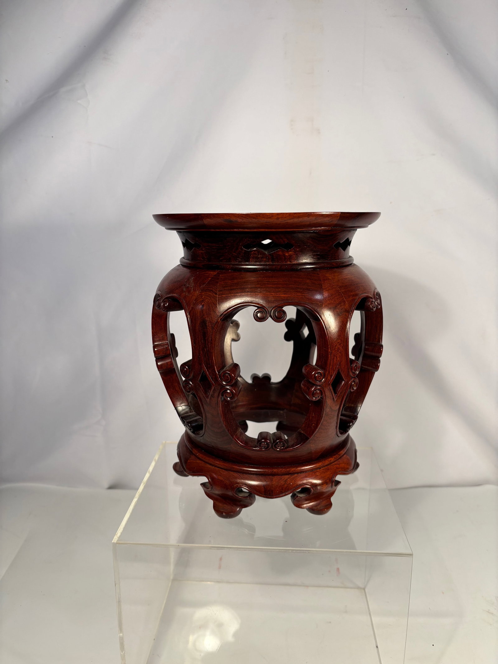A Chinese Carved rosewood Stand: 19th century; Chinese carved rosewood display stand of cylindrical form, featuring pierced openwork panels with scrolling and geometric motifs, raised on short bracket feet. The top is recessed to