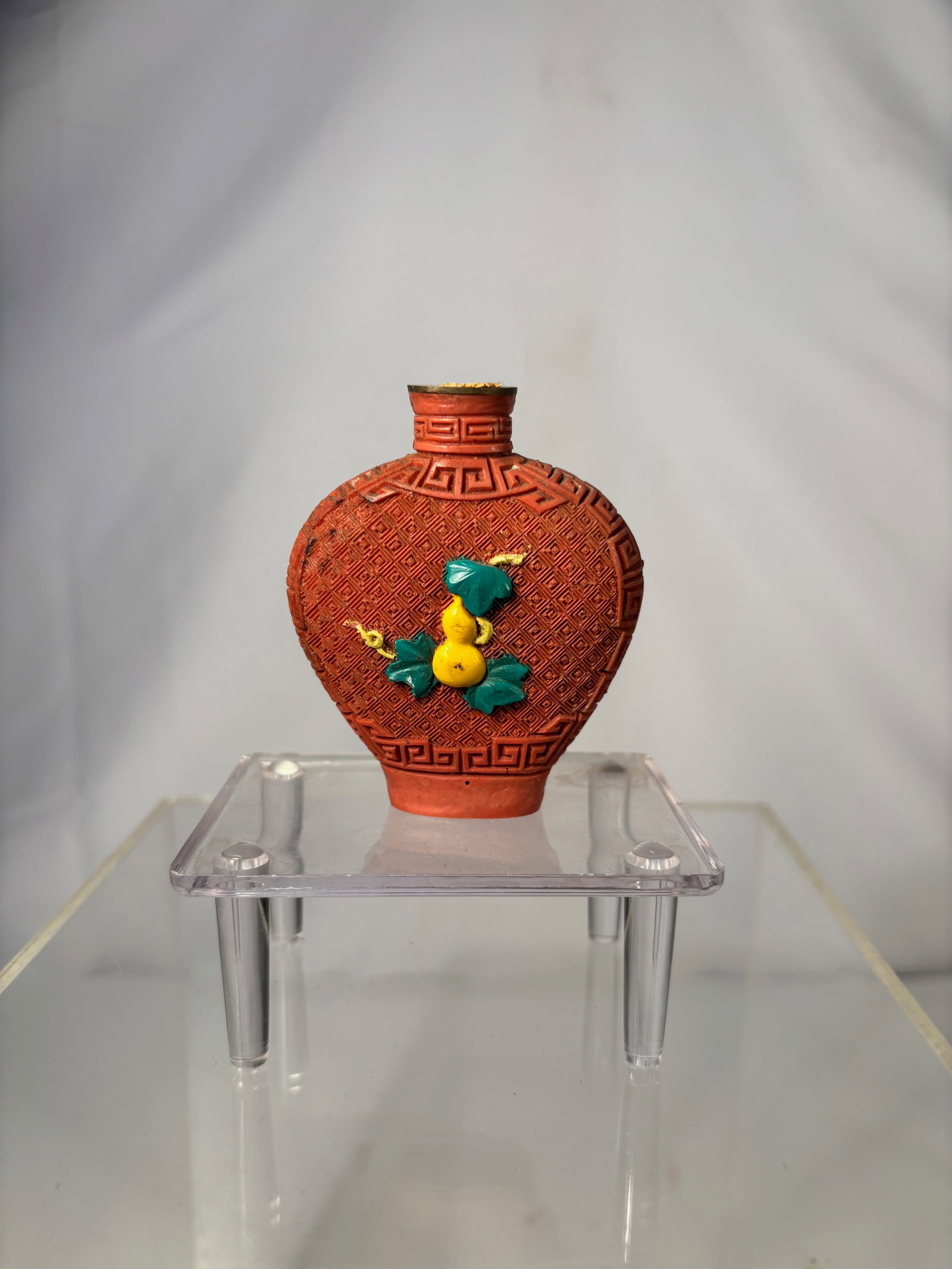 A Chinese Cinnabar-Style Snuff Bottle with Double Gourd Motif, 20th Century: Molded cinnabar-style snuff bottle of flattened ovoid form, decorated overall with a repeating leiwen (thunder) pattern and applied with a raised double gourd and leafy vine motif in contrasting