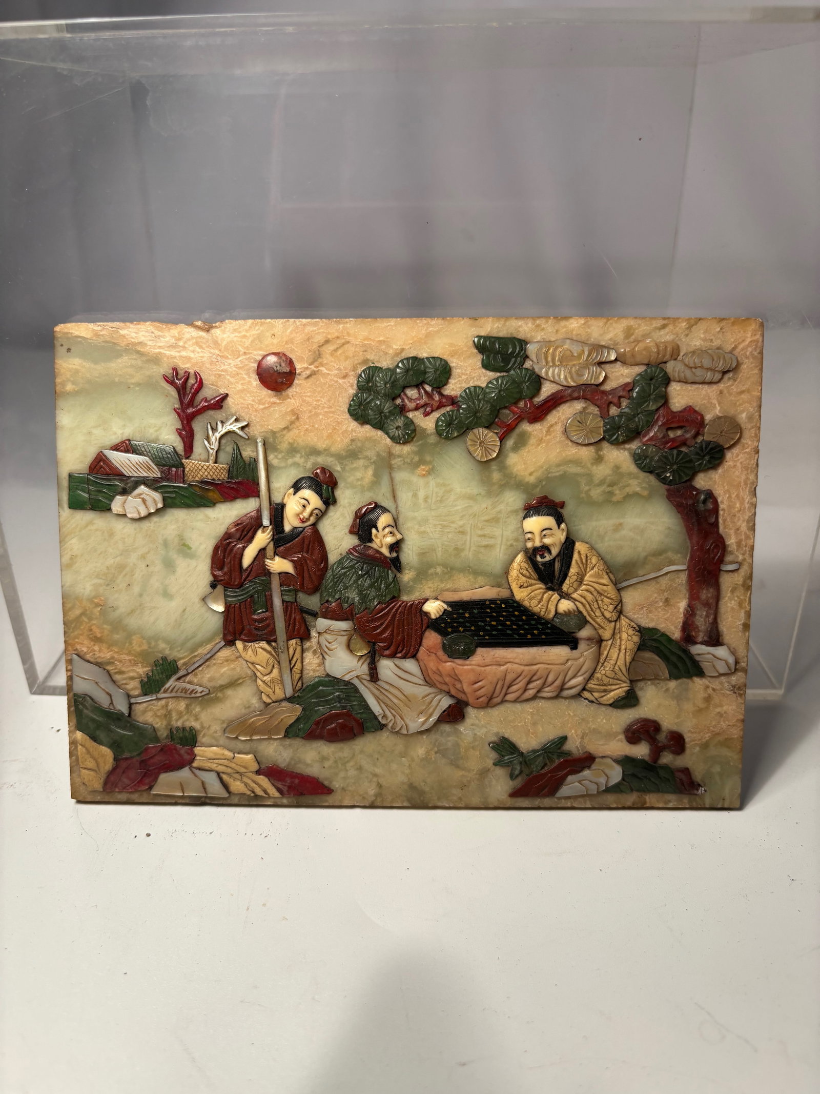 A Fine Chinese Carved and Inlaid Jade Panel: Qing dynasty(1644-1912); A rectangular jade and hardstone inlaid panel finely depicting three scholars engaged in a game of weiqi (Go) beneath a spreading pine tree, an attendant standing nearby holdi