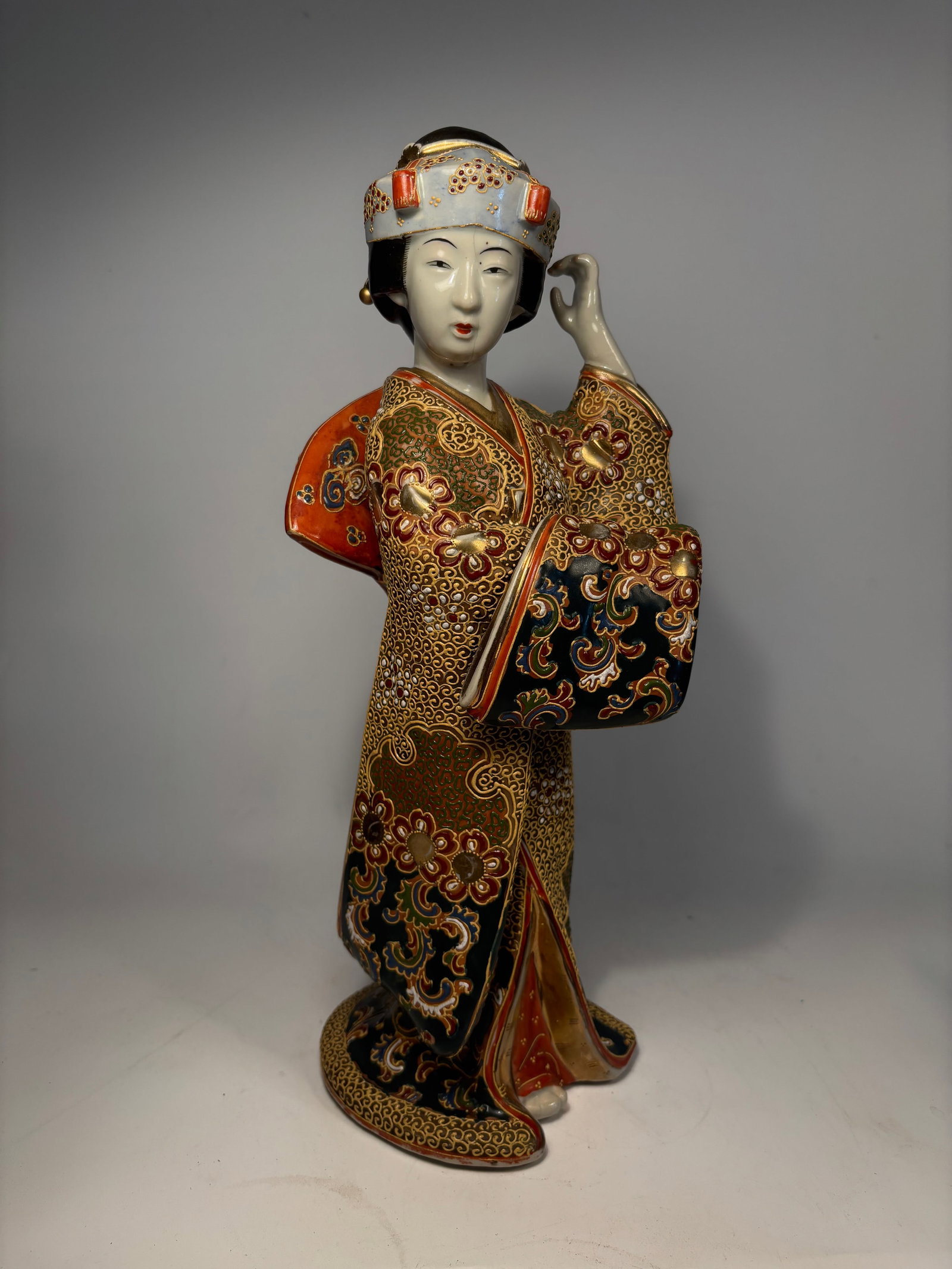 A Japanese Satsuma Moriage Porcelain Geisha Figure: Meiji Period(19th century); A finely modeled and richly decorated Japanese porcelain figure of a Geisha, dating to the Meiji period (late 19th century). The figure is adorned in an elaborate kimono wi