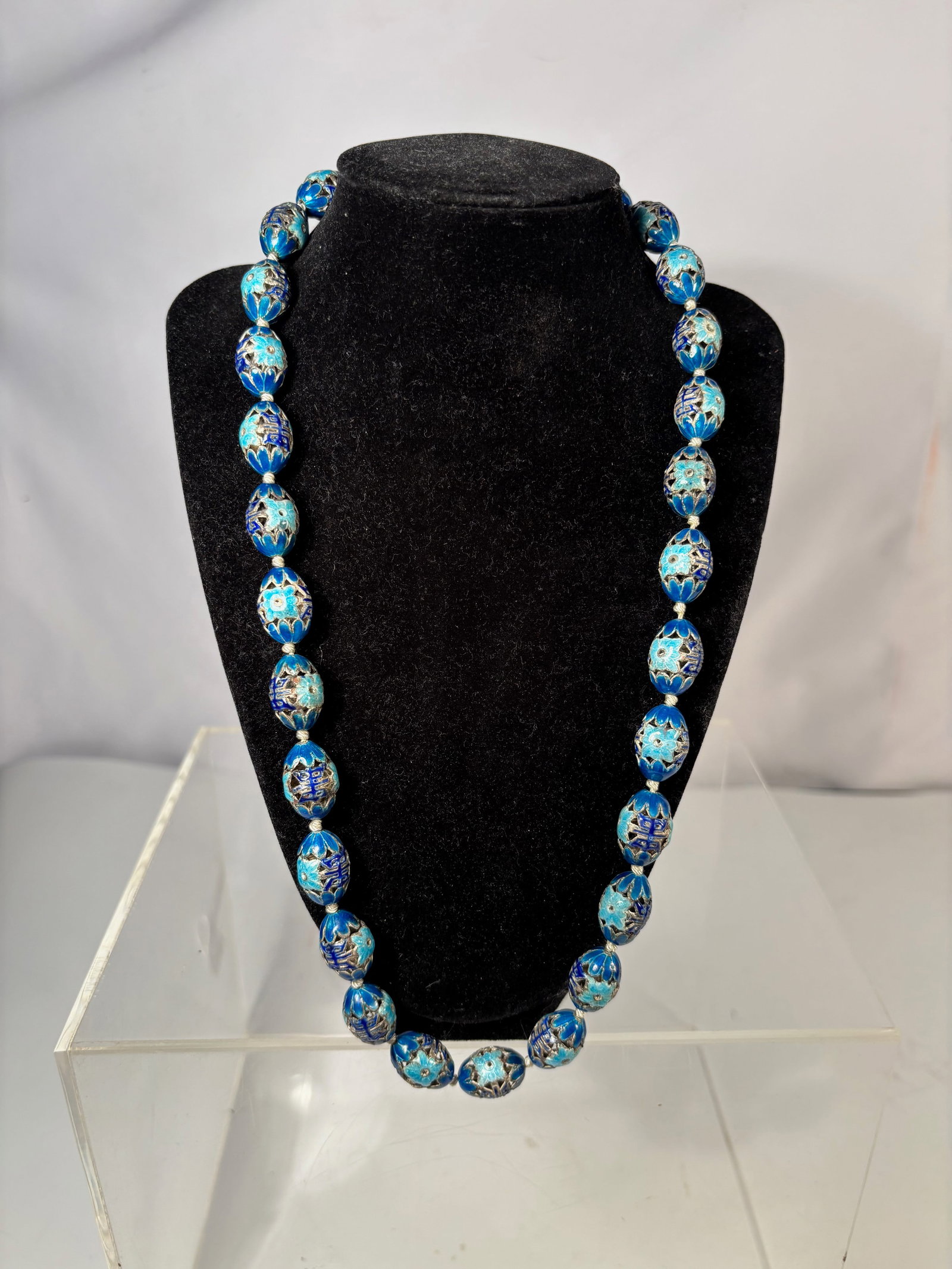 A Chinese Silver Cloisonné Enamel Bead Necklace, 19th century: Chinese necklace composed of graduated silver cloisonné enamel beads decorated with floral motifs in blue tones, strung with small spacer beads and fitted with a metal clasp. Length: 25 inches.