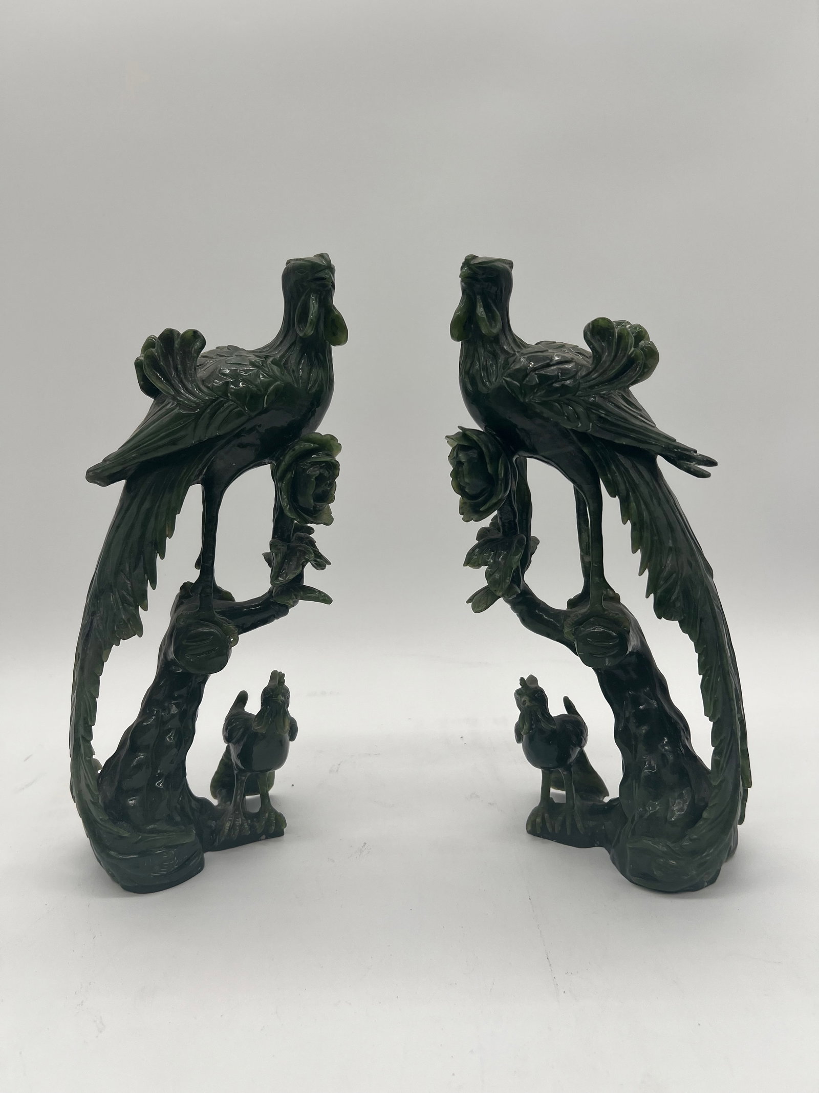 A pair of Chinese green jade bird sculptures: Late 19th century to early 20th century; The carvings depict birds, likely phoenixes or peacocks, perched on trees with human figures at the base. Dimensions?Height: 10.5 inches