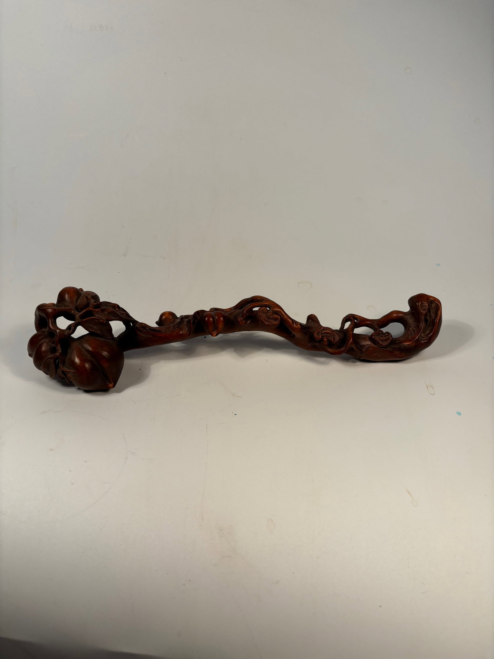 A Chinese carved boxwood or hardwood ruyi scepter: Qing Dynasty (1644-1912); The head is carved in the shape of a lingzhi fungus with additional auspicious elements like peaches and vines, symbolizing longevity and prosperity.Dimensions? Length: 11.5
