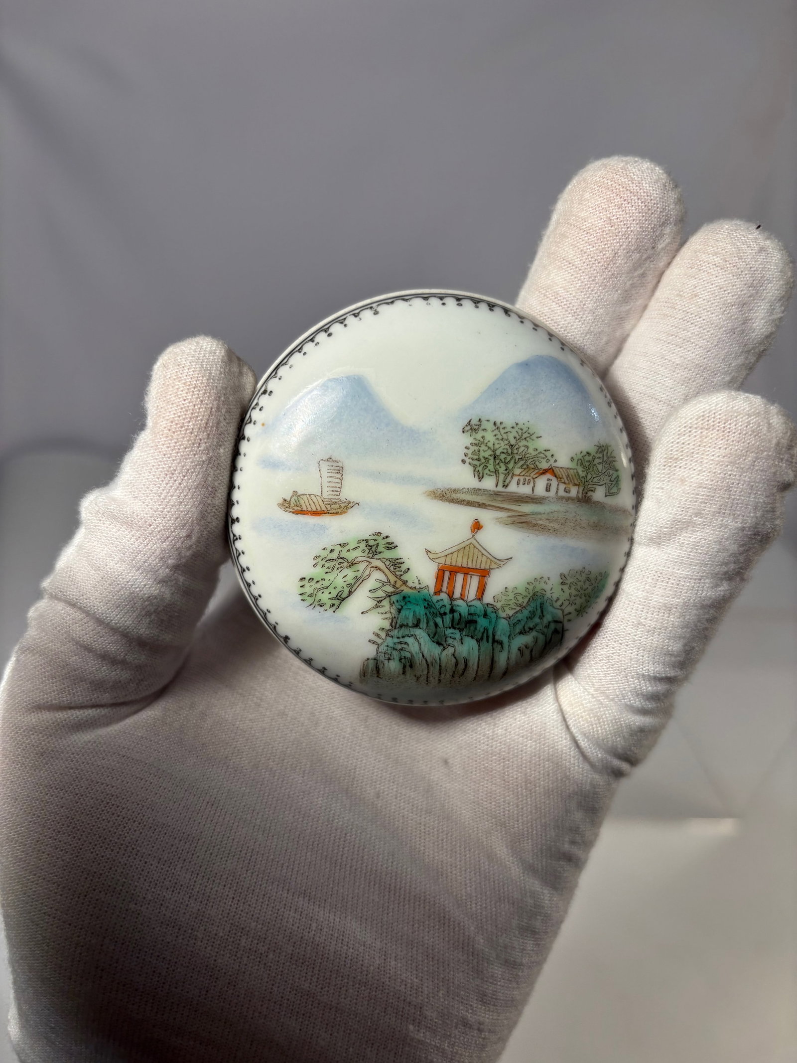 A Chinese Porcelain Covered Box with Landscape Decoration, Yongzheng Mark: Chinese porcelain covered box decorated with a landscape scene including a pavilion, trees, and a boat. The base bears a red apocryphal Yongzheng mark. Diameter: 2.75 inches; Height: 1.25 inches.