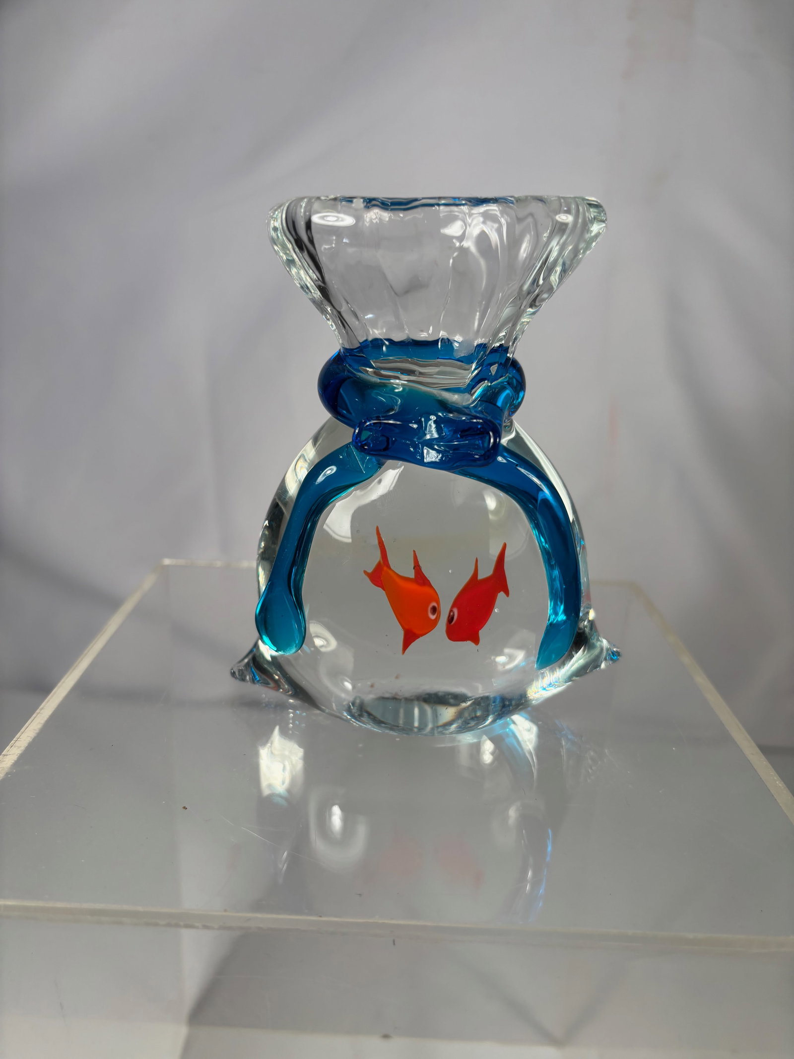 An Art Glass Goldfish in Bag Sculpture: Decorative art glass paperweight in the form of a goldfish bag, featuring two red fish encased in clear glass with blue glass accents forming the tied bag design. Height: 5 inches; Length: 4 inches.