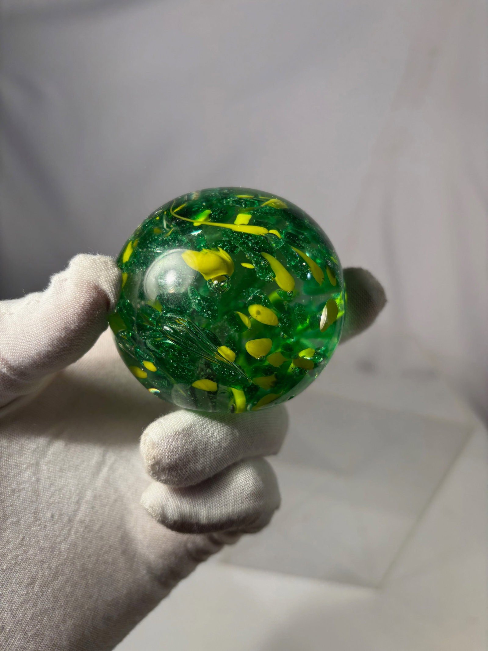 Murano Style Art Glass Paperweight, Green & Yellow Abstract Design: This decorative art glass paperweight features a rounded, polished form with a vibrant green body accented by scattered yellow inclusions. The abstract pattern creates a lively, confetti-like effect s