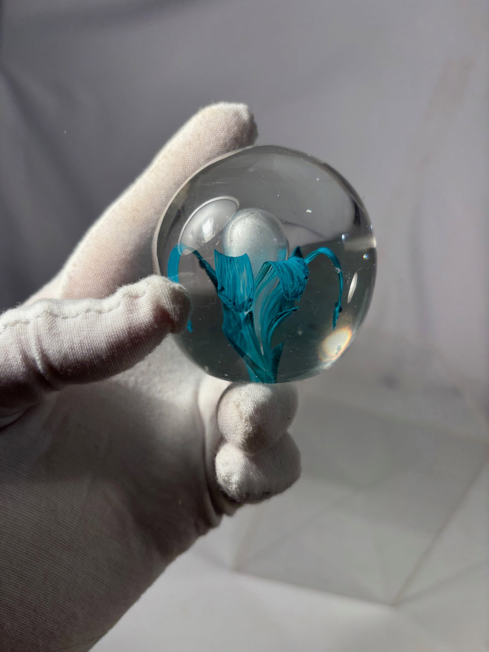 Studio Art Glass Paperweight w/ Teal Blue Ribbon & Bubble Design: A hand-blown studio art glass paperweight featuring elegant teal blue ribbon-like forms encased within a clear glass sphere. The design incorporates controlled internal movement with a central bubble