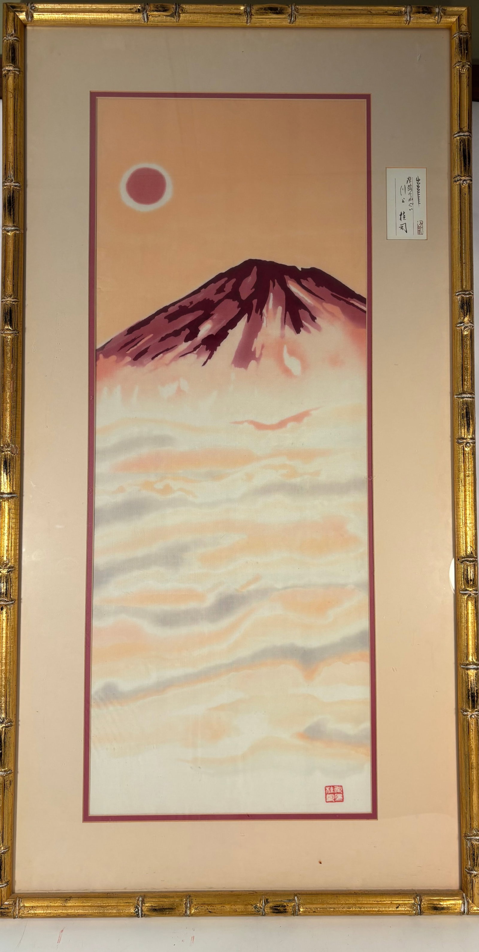 A Japanese Silk Painting of Red Fuji, Signed Kawakami Keiji: A finely executed Japanese silk painting depicting the iconic Red Fuji beneath a crimson sun, rising above a softly rendered sea of clouds. The composition is presented in warm shades of pink, cream,