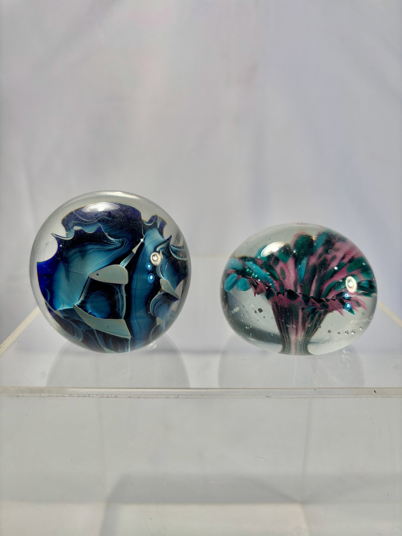 Lot of Two Studio Art Glass Paperweights, Abstract Floral & Swirl Designs: A group of two vintage studio art glass paperweights, each with vibrant internal sculptural designs. One features a pink, teal, and white swirling floral burst with controlled bubbles; the other displ
