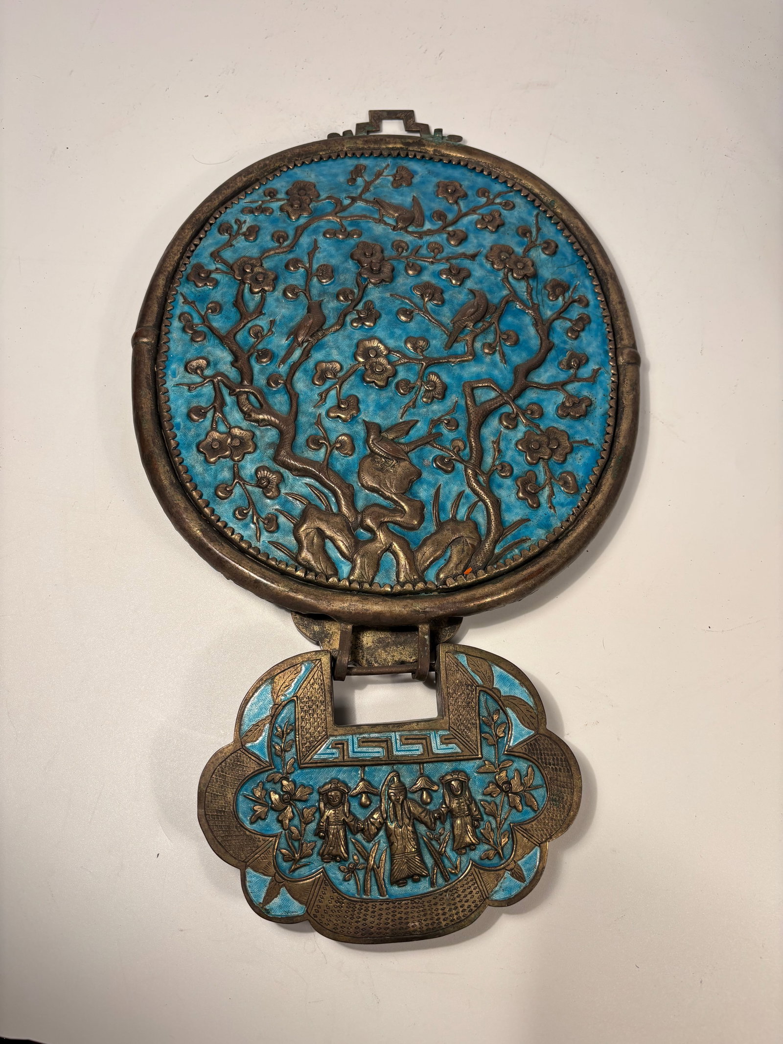 A Chinese Cloisonné Enamel and Gilt Bronze Mirror with Auspicious Inscription: Qing Dynasty (1644-1912); Of circular form, the mirror set within a gilt bronze frame finely decorated in turquoise-blue cloisonné enamel with stylized floral scrolls, surmounted by a geometric loop.
