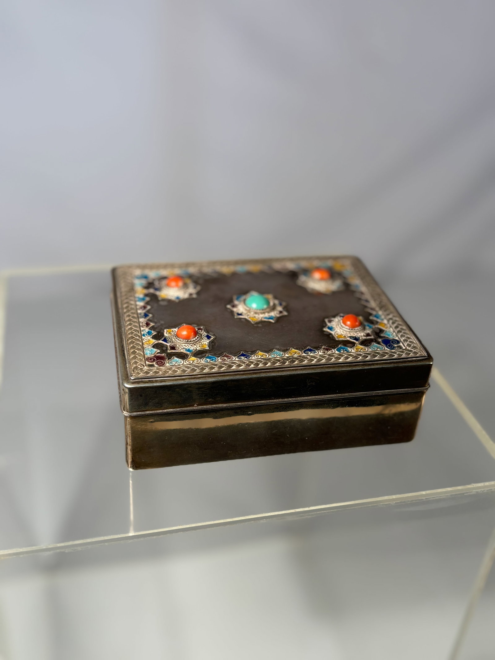 A Chinese Silver and Zitan Box with Coral, Turquoise, and Cloisonné Enamel Inlay: Rectangular silver box with zitan wood base and lining, the cover richly decorated with four coral cabochons and a central turquoise cabochon, each set within intricate star-shaped mounts of multicolo