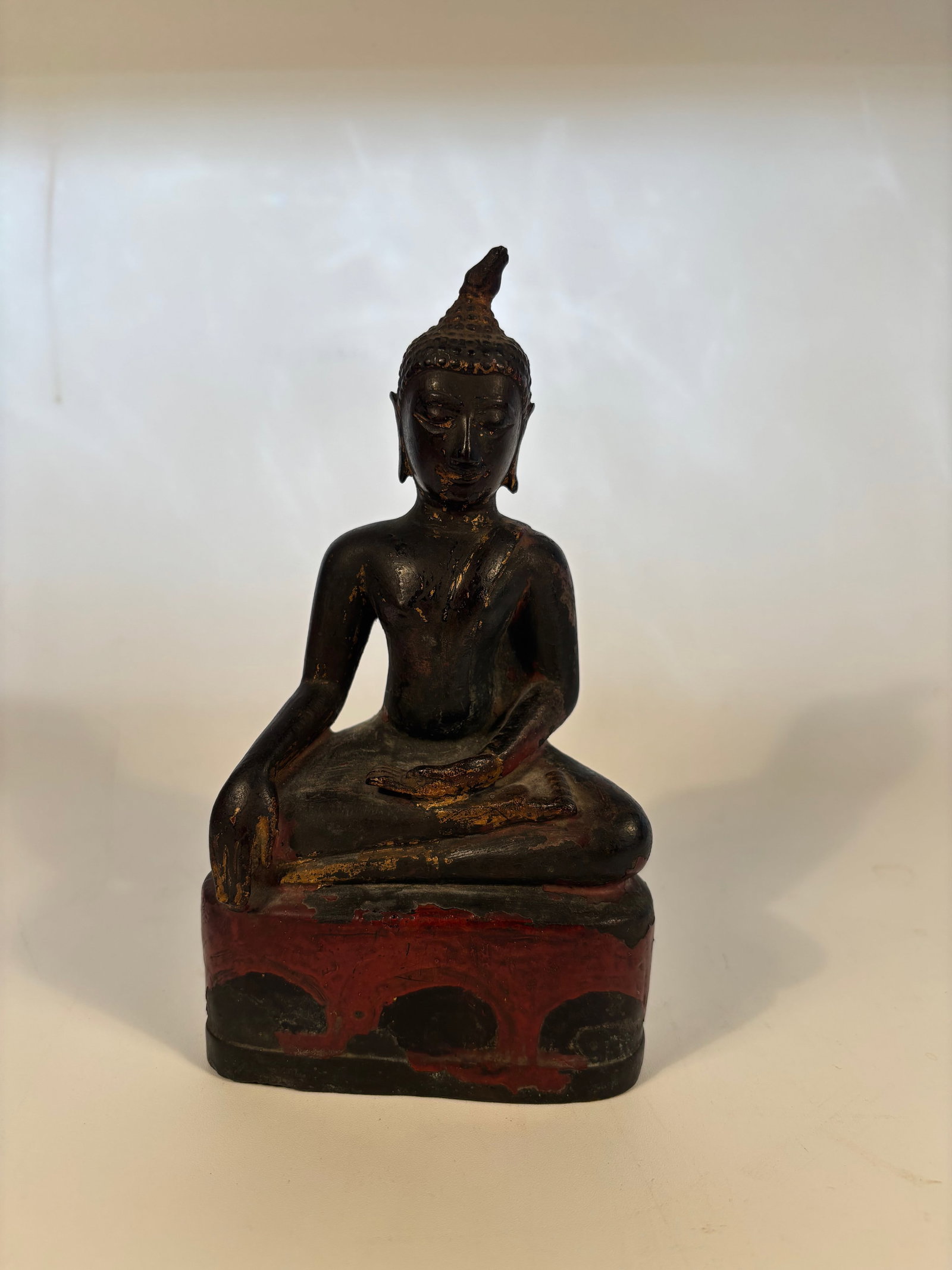 An asian seated bronze buddha statue: 17th century to 18th century ; The Buddha is seated in dhyana (meditation) with one hand in the earth-touching gesture, symbolizing the moment of enlightenment. Traces of original gilt and red