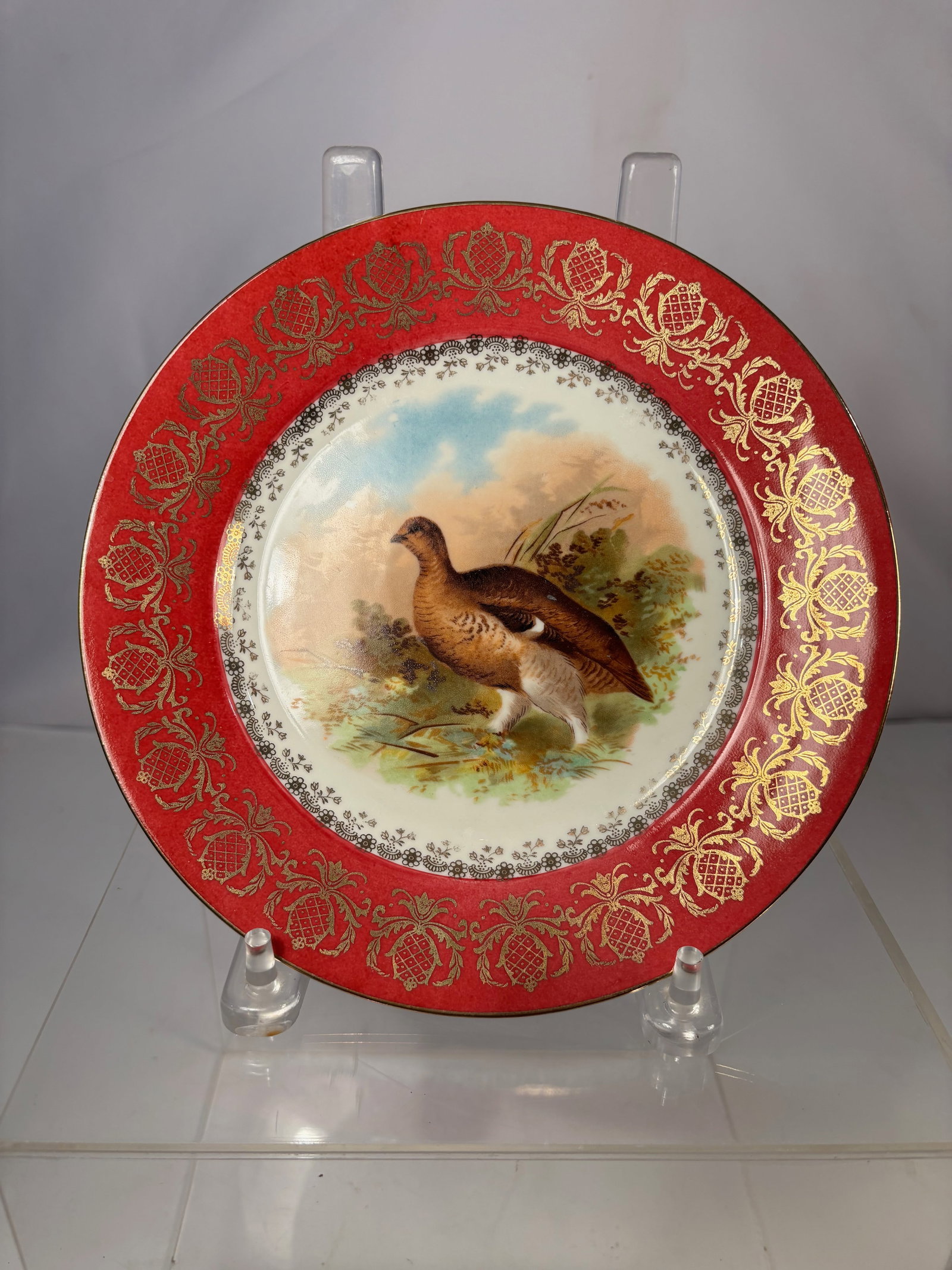 An Austrian Porcelain Cabinet Plate with Hand-Painted Game Bird: Austrian porcelain cabinet plate, late 19th to early 20th century, decorated with a finely hand-painted game bird within a landscape setting. The wide red ground border is richly embellished with gilt