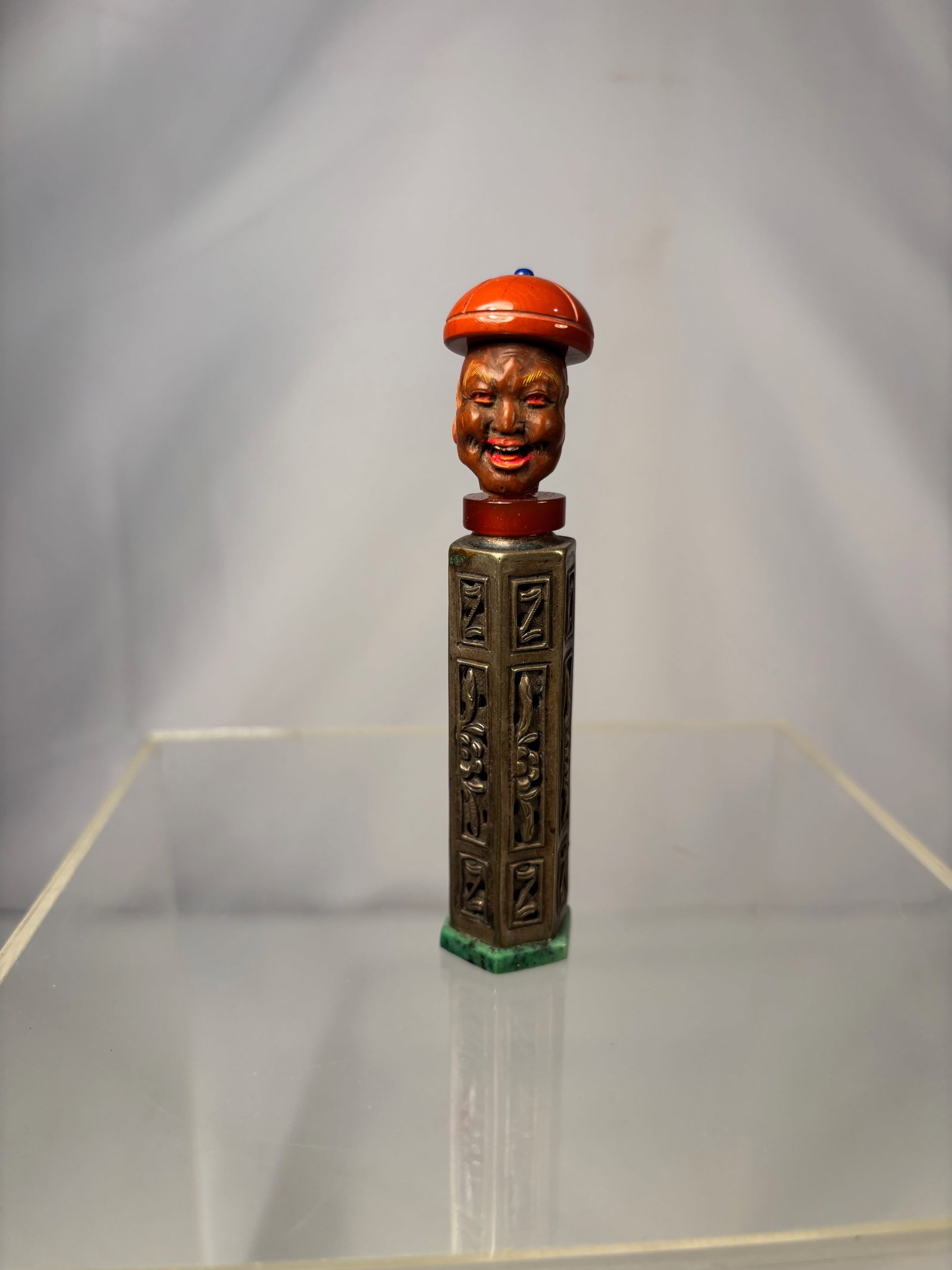 A Chinese composite snuff bottle, late Qing dynasty, circa 1880–1920: The bottle with a silver body, cast and chased in archaistic panel form, raised on a hexagonal green hardstone base (likely nephrite or serpentine). The neck fitted with a red stone or glass collar.