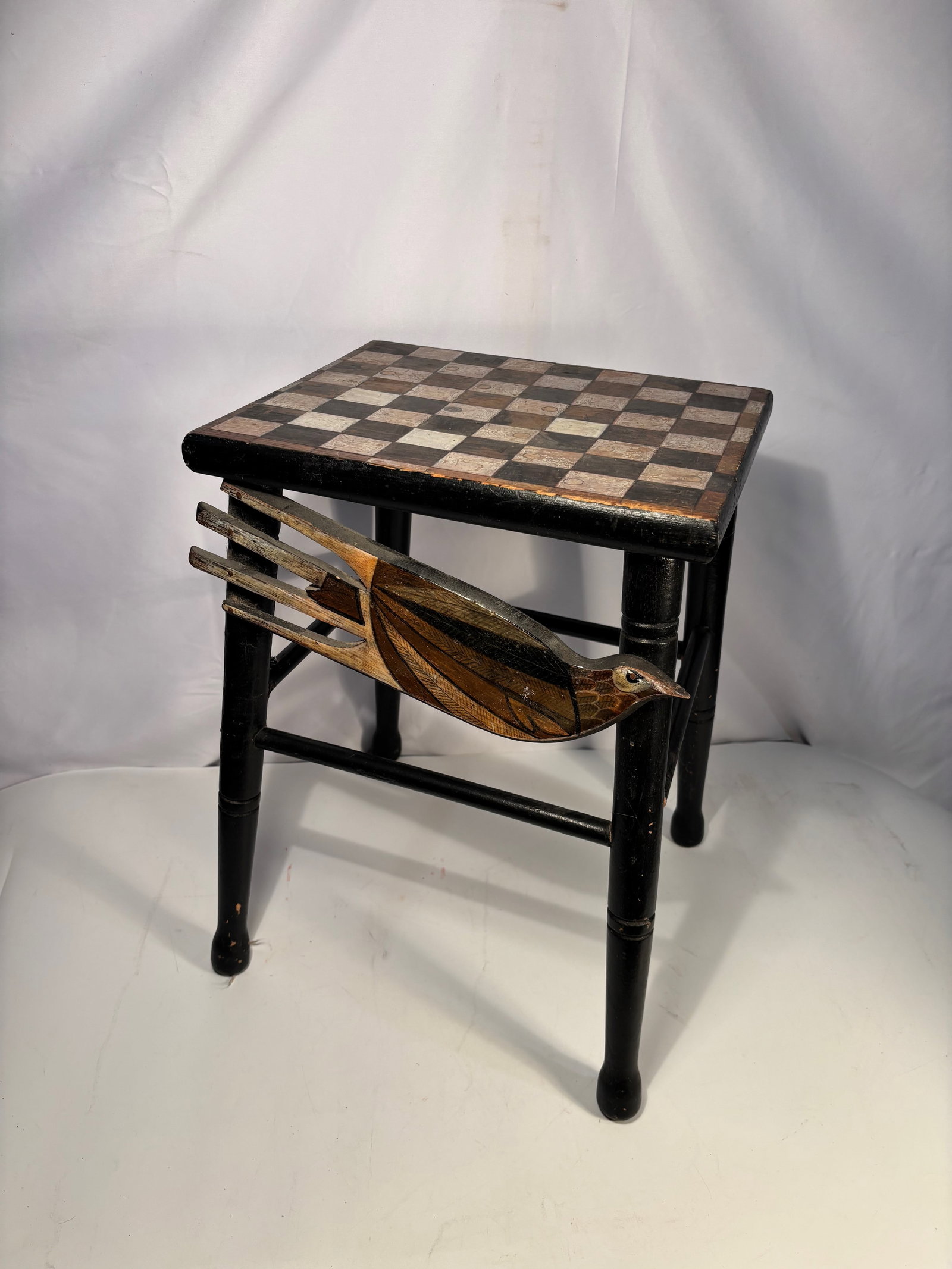 Folk Art Game Table with Checkerboard Top and Carved Bird Motif: Decorative folk art table featuring a checkerboard game top above a painted and carved bird motif mounted to the apron. The bird is rendered in layered wood with carved detailing to the body, wing, an