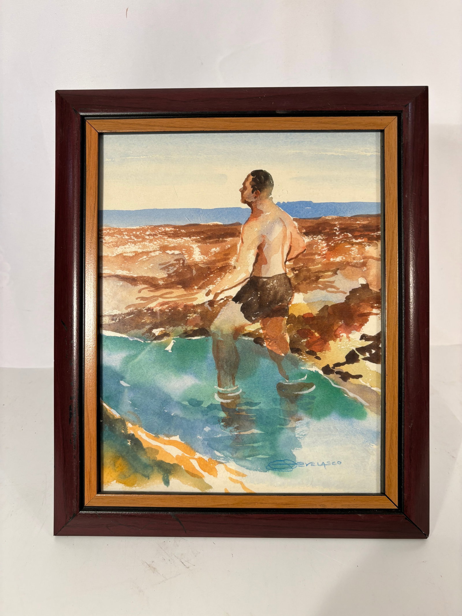 Signed J. Velasco Watercolor of Figure in Coastal Pool: A striking signed J. Velasco watercolor depicting a lone male figure standing ankle-deep in a vivid turquoise tidal pool or coastal inlet. Rendered in warm earth tones and loose expressive washes, the